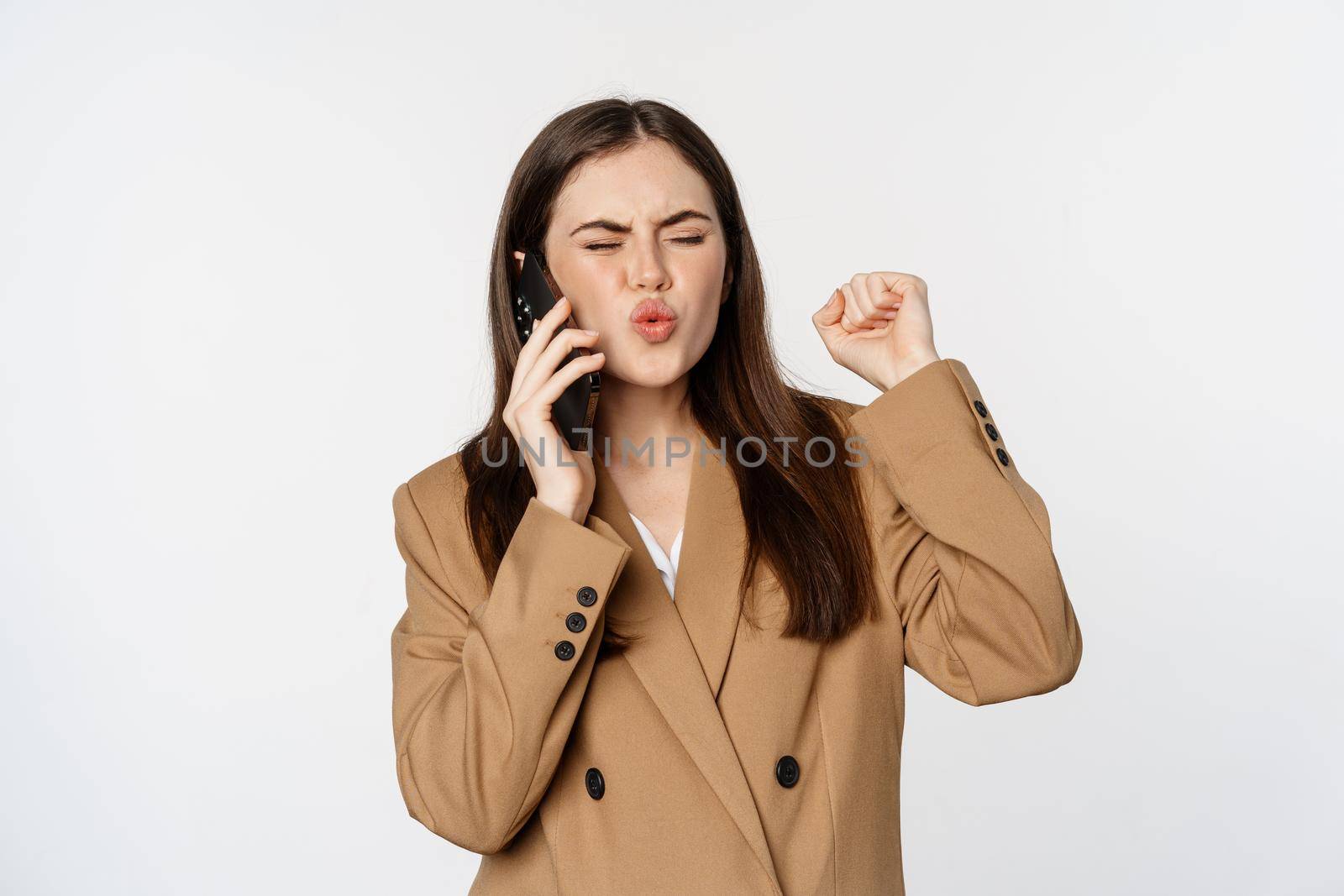 Enthusiastic businesswoman talking on mobile phone, reacting amazed and happy to call, recieve great news, standing over white background.