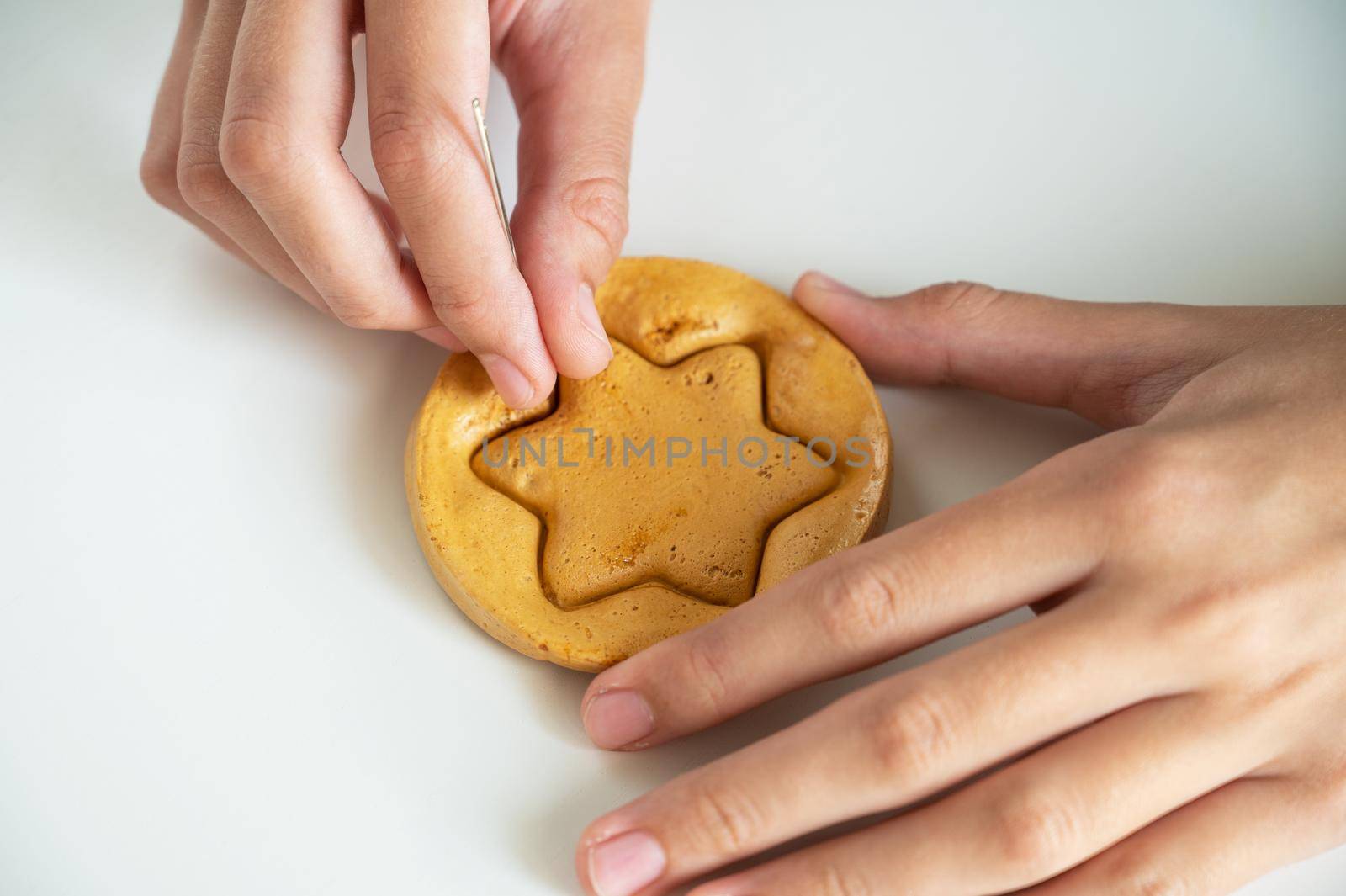 Hands closeup scratch brown sugar caramel candy cookies with a metal needle in the shape of a star on a white background.
