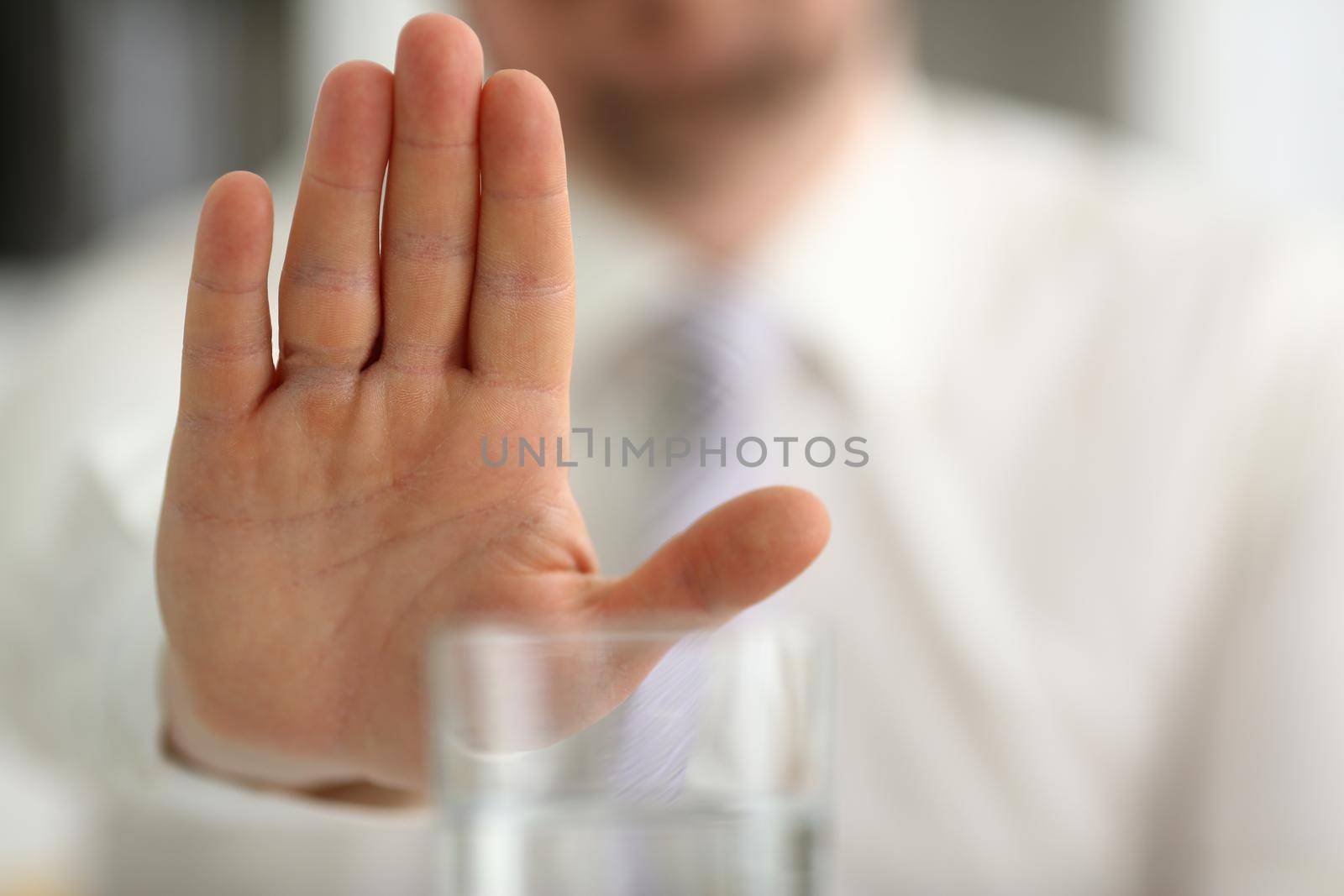 Male hand shows a negative gesture to glass beaker. Refusal of spicy alcoholic drinks concept