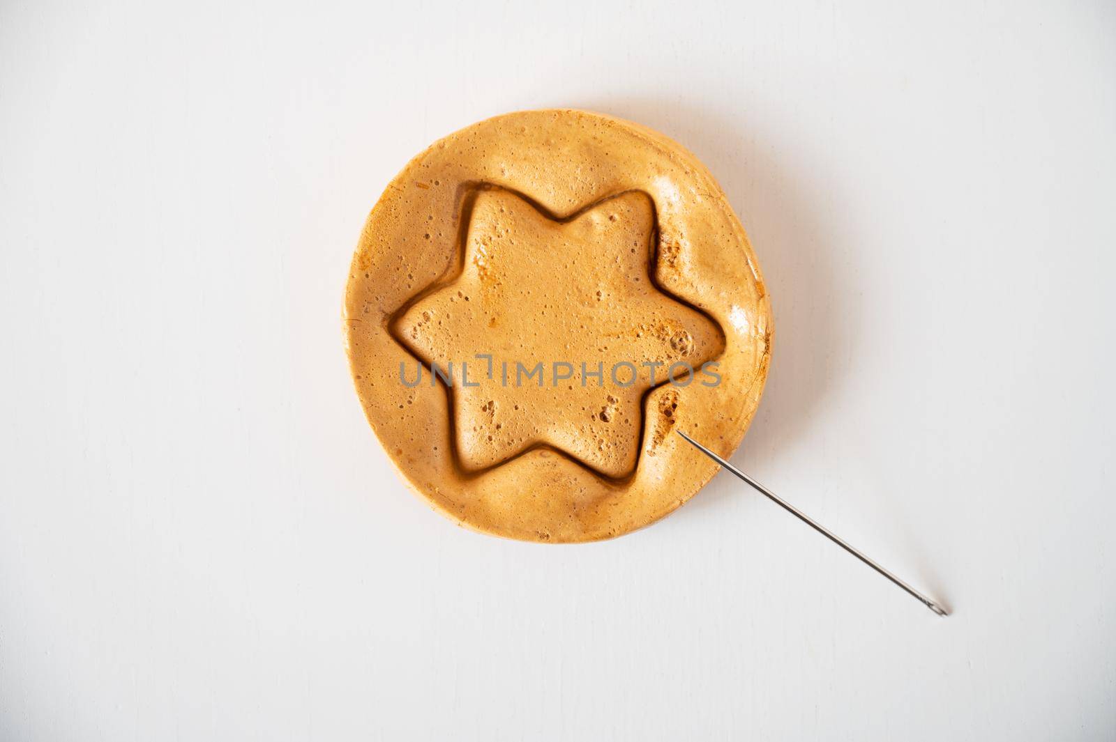 Brown sugar caramel candy cookies with a metal needle in the shape of a star on a white background.
