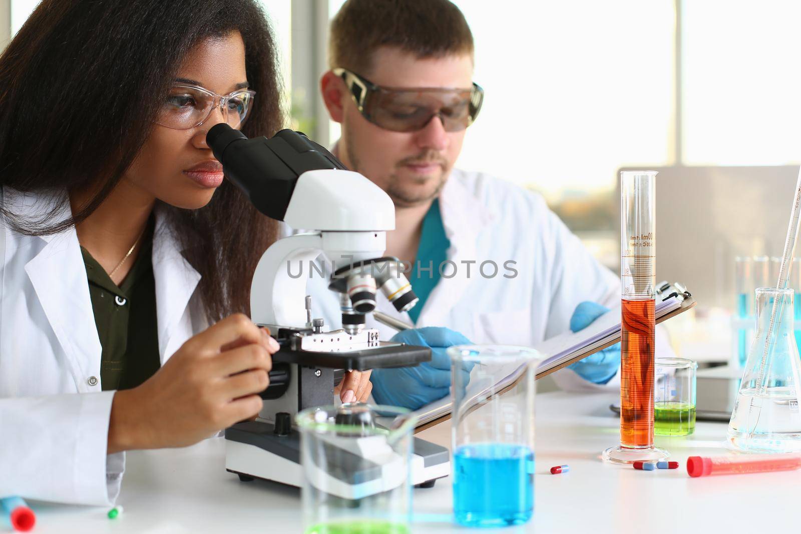 Two chemistry students conduct microscopic examinations in laboratory. Scientific research in chemical industry concept