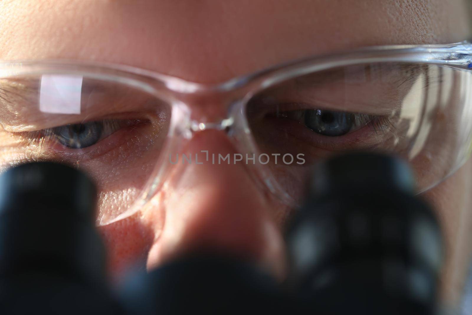 Male scientist looks through binocular microscope and studies disease of virus. Health care and research concept