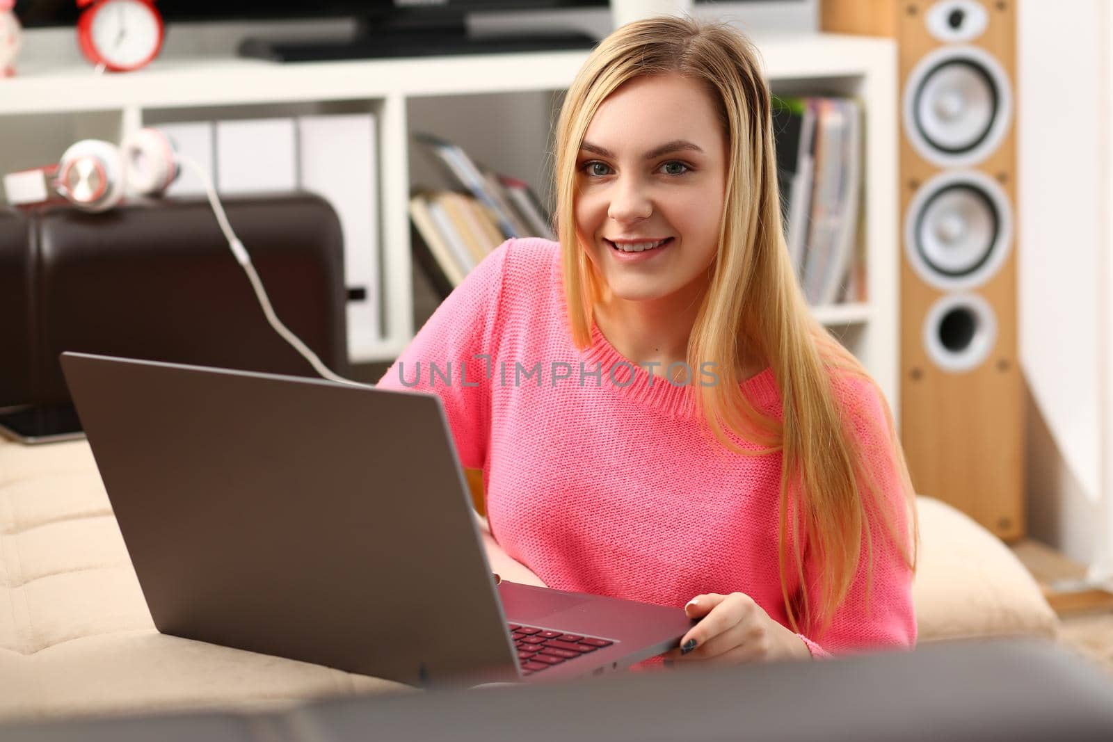 Young smiling blonde woman sitting in living room working on laptop. Remote work and freelance concept