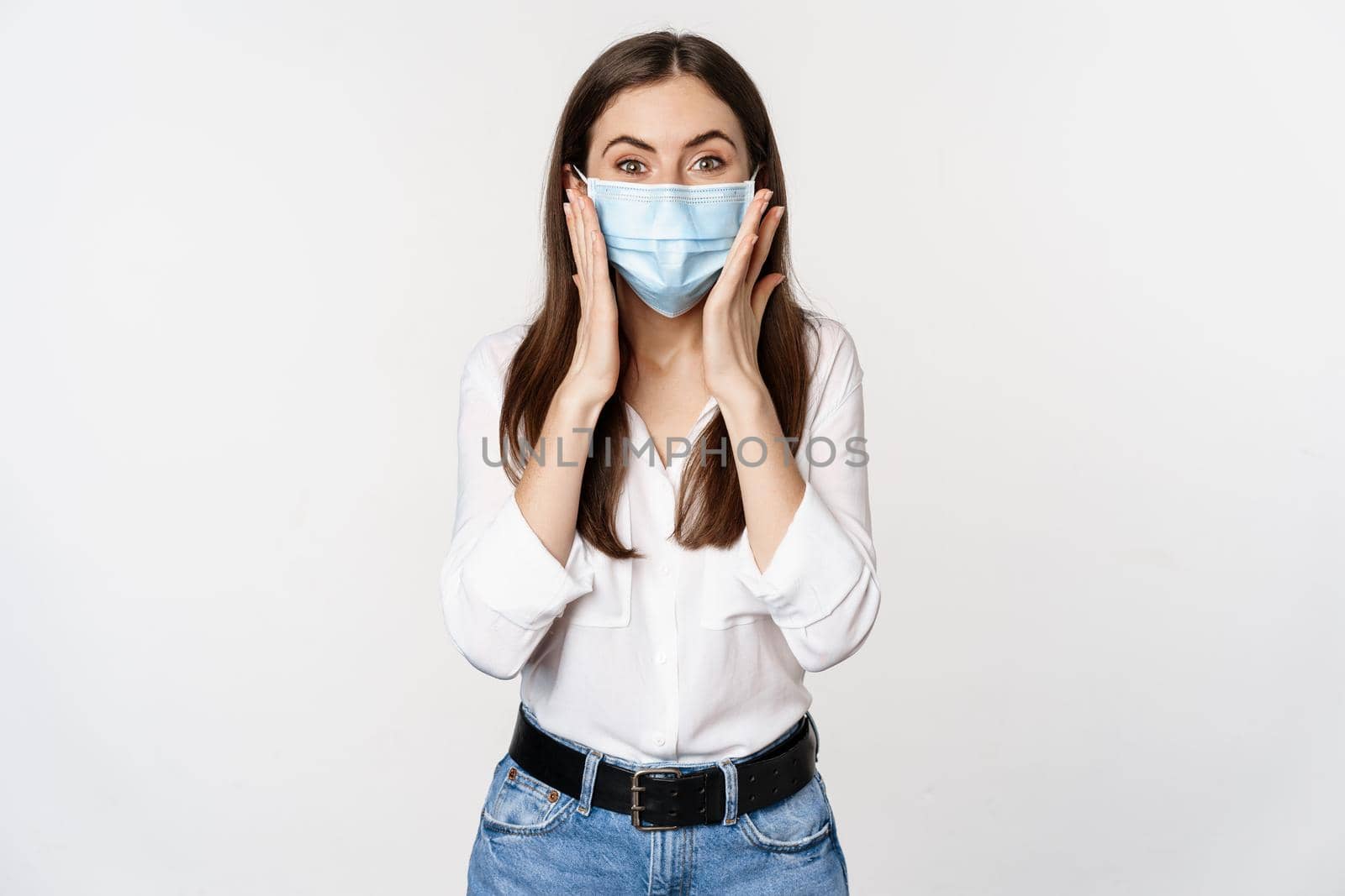 Surprised woman in face medical mask looking amazed, checking out awesome news, big reveal, standing over white background.