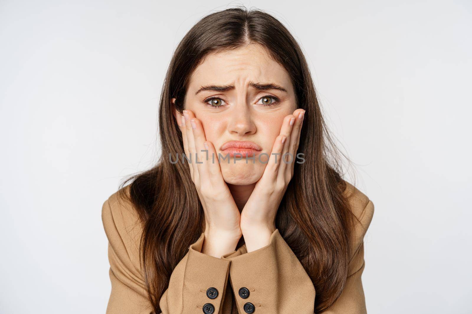 Image of sad girl looking in mirror and touching facial skin, shocked and frustrated over bad skin condition, standing over white background.