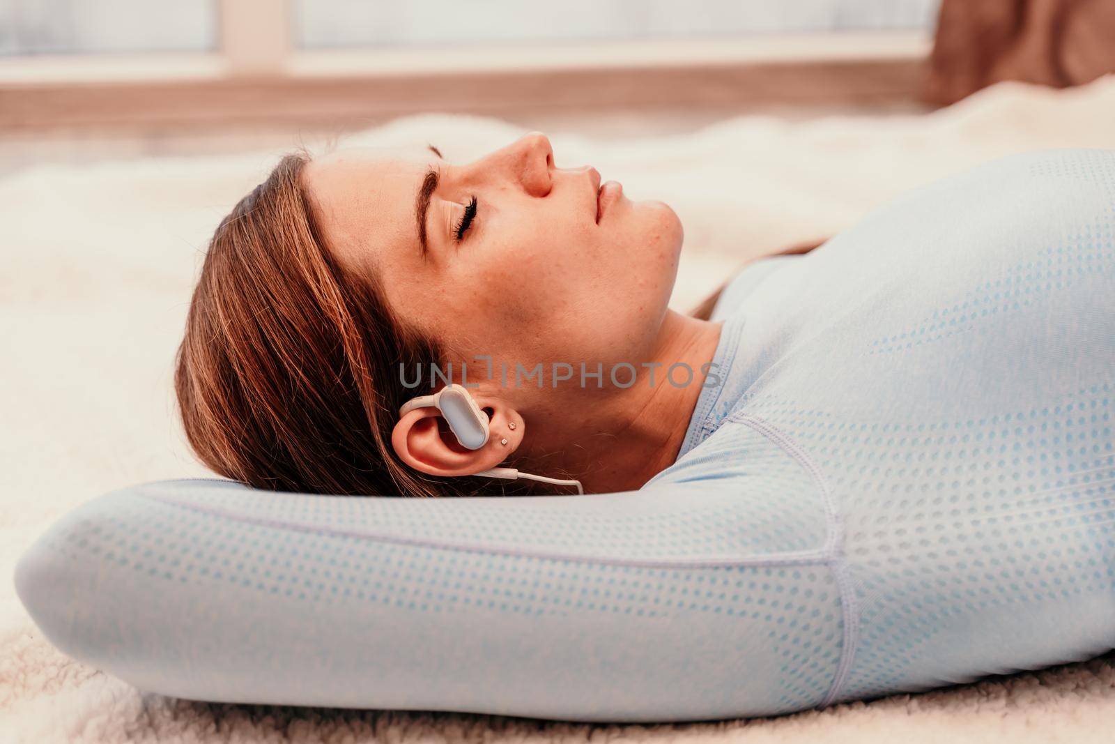 Side view portrait of a relaxed woman listening to music with headphones lying on a carpet at home. by Matiunina