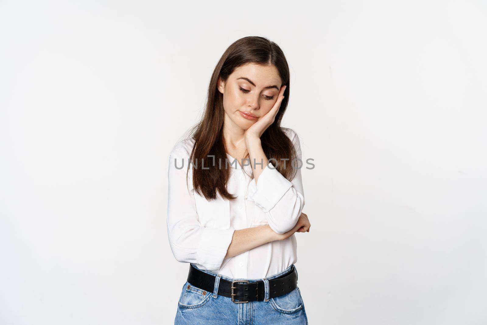Unamused, bored brunette woman looking gloomy and sad, sighing, standing reluctant over white background.
