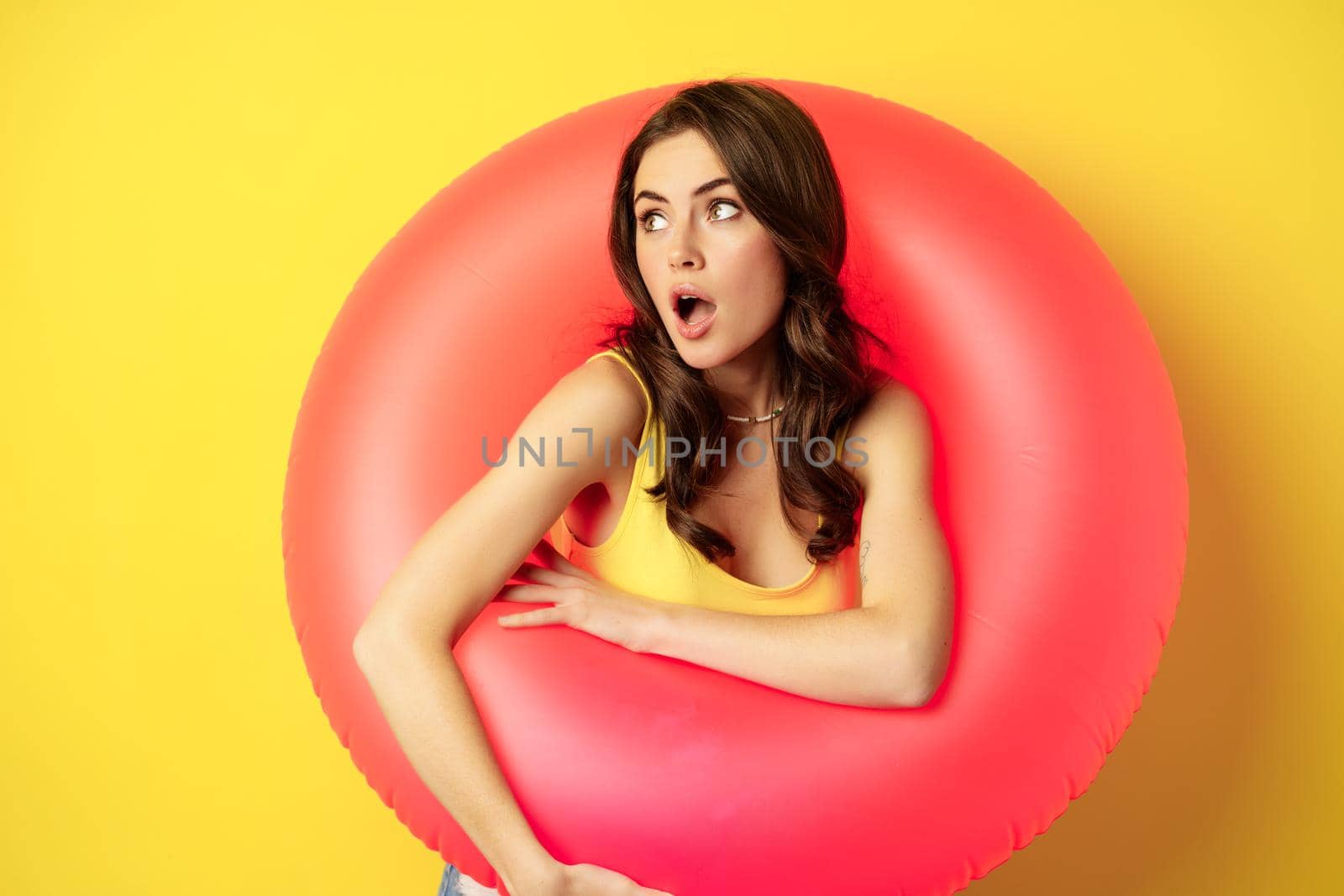 Close up portrait of coquettish young sexy woman inside pink swimming ring, concept of beach holiday, vacation and summer, yellow background.