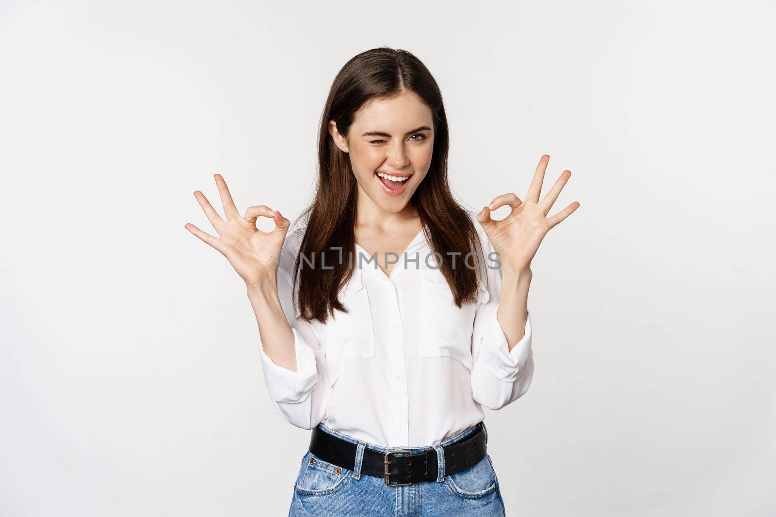 Smiling confident business woman, winking, showing okay ok sign, excellent, no problem gesture, standing over white background.