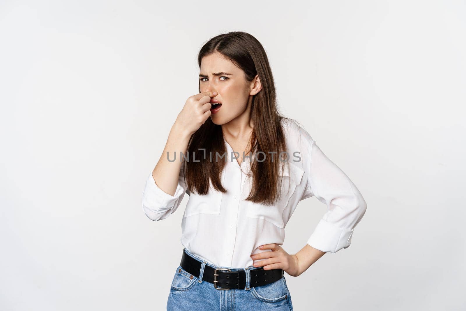 Disgusted adult woman, 25 years old, shut nose from dislike and disgust, bad smell, standing over white background. Copy space