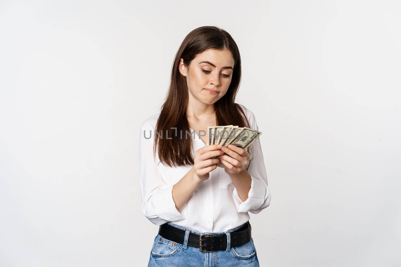 Sad woman counting money, lacking cash, standing gloomy over white background.