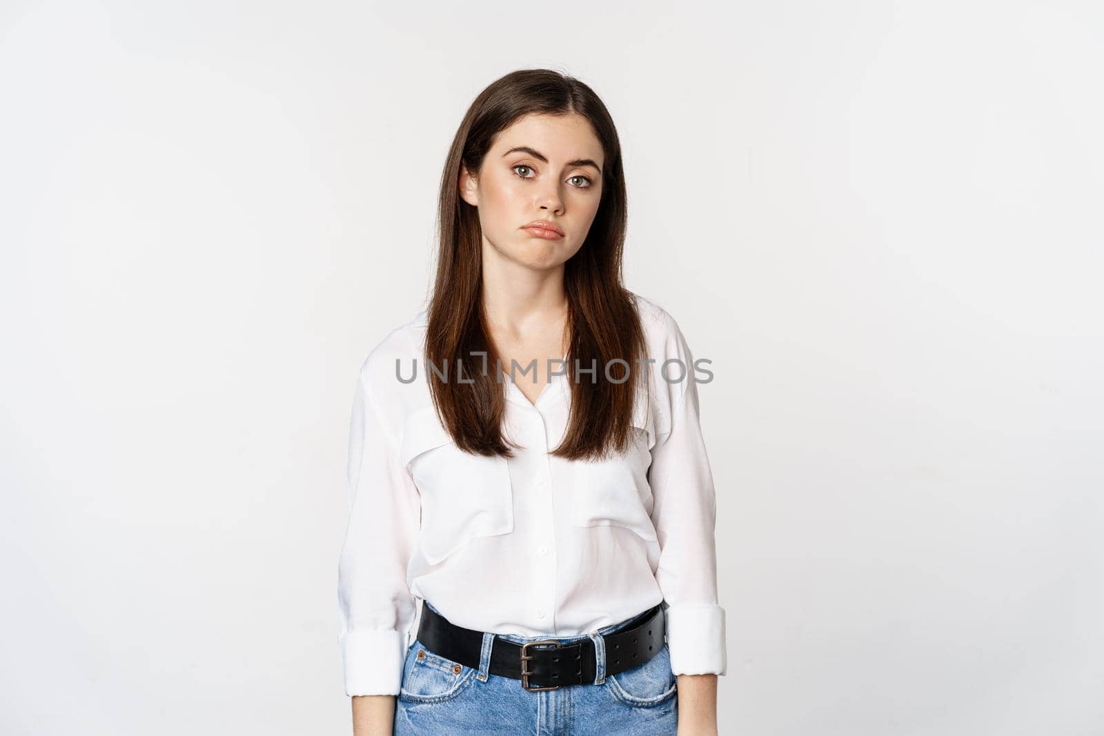 Sad and gloomy woman sulking, looking disappointed and moody, standing upset against white background.