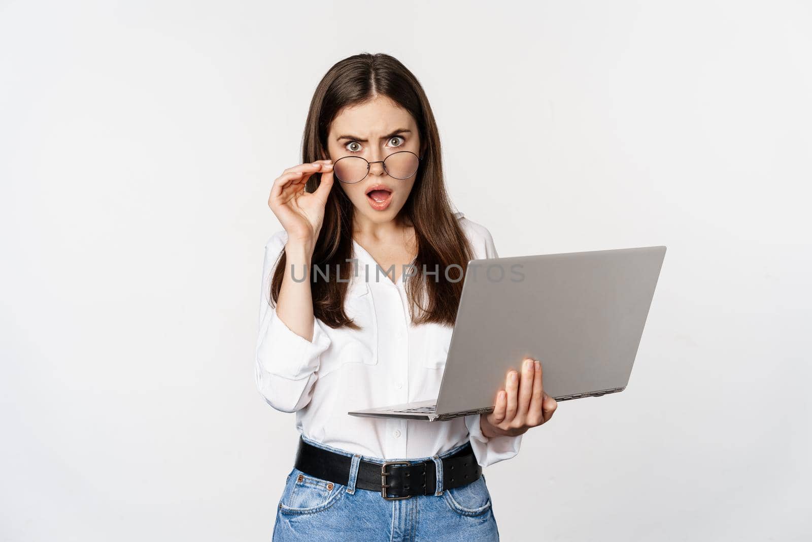 Shocked woman looking at laptop screen confused, stunned about smth on computer, standing over white background.