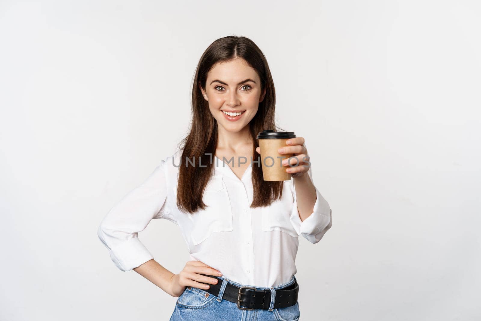 Image of modern woman, office lady holding takeaway coffee cup and smiling, standing over white background.
