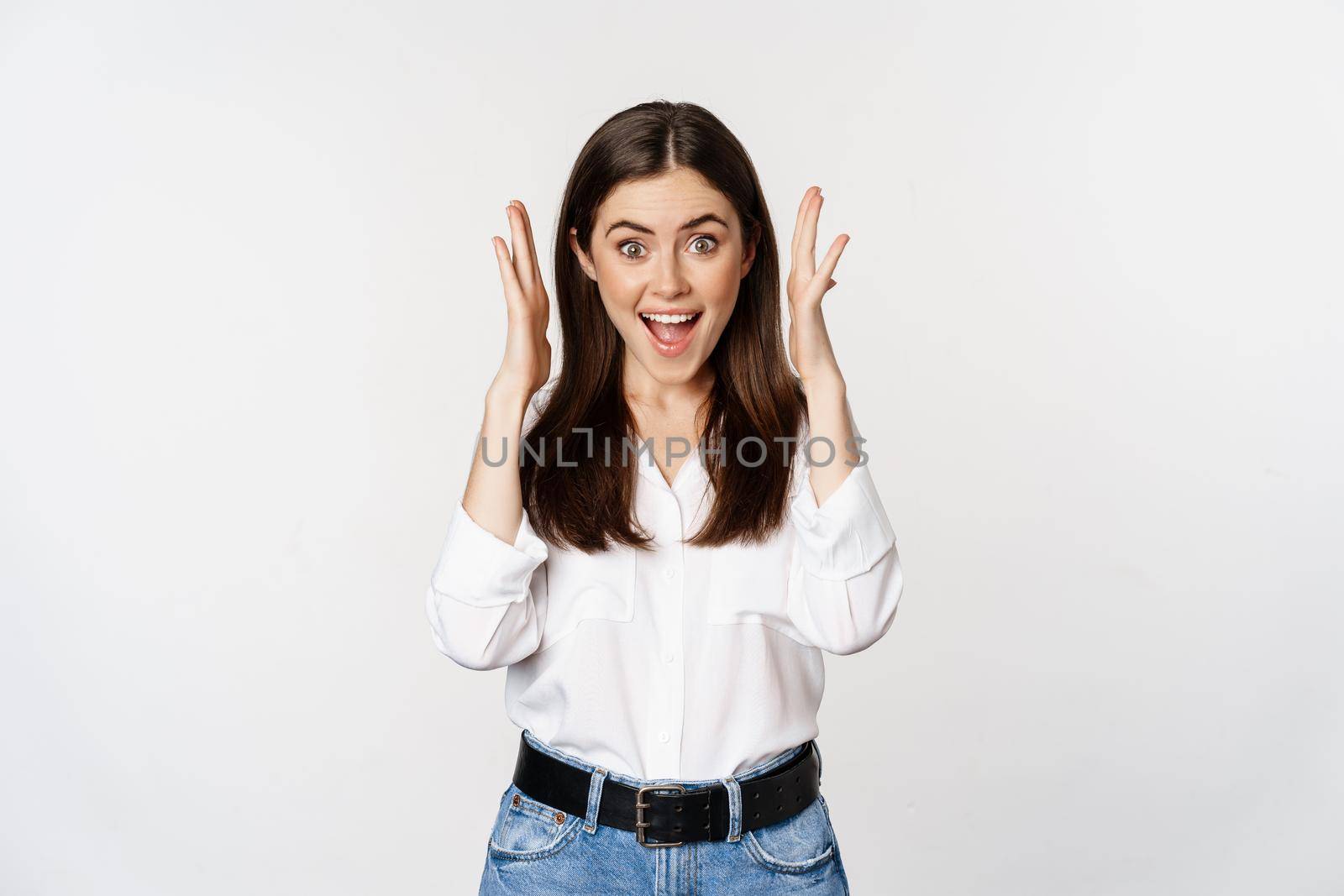 Excited young adult woman reacting to win, surprise news, screaming and cheering, triumphing, achieve goal and celebrating, standing over white background.