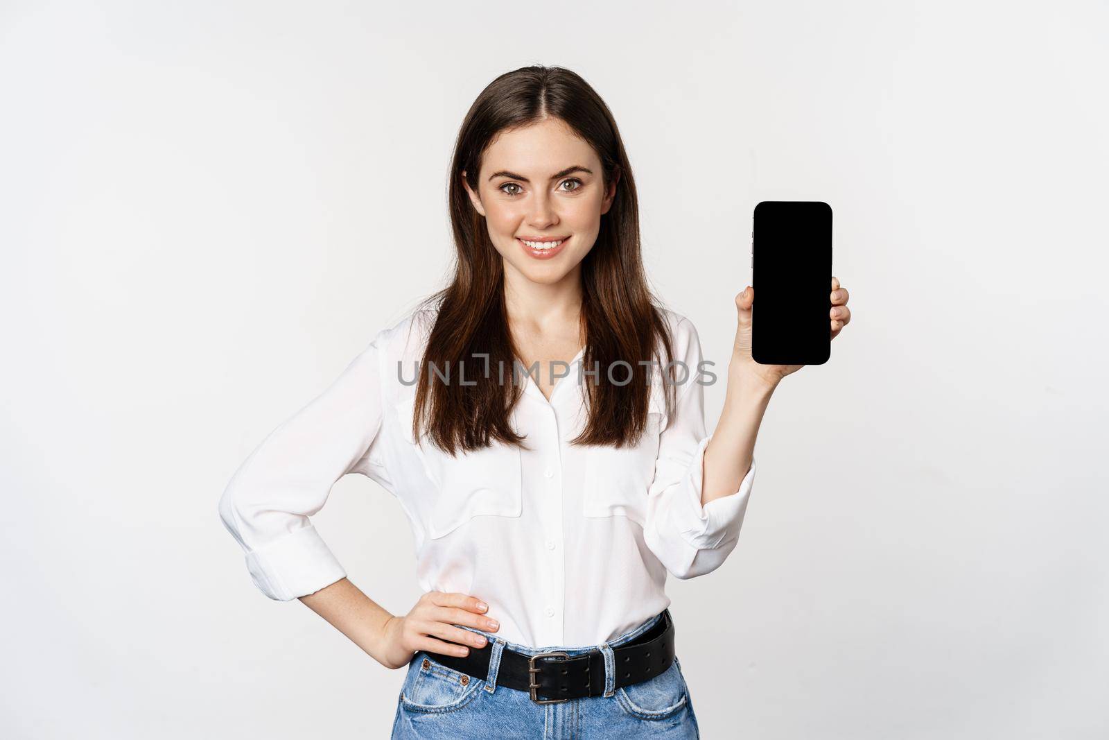Confident woman in corporate clothes, showing smartphone screen, mobile interface of an application, standing over white background.