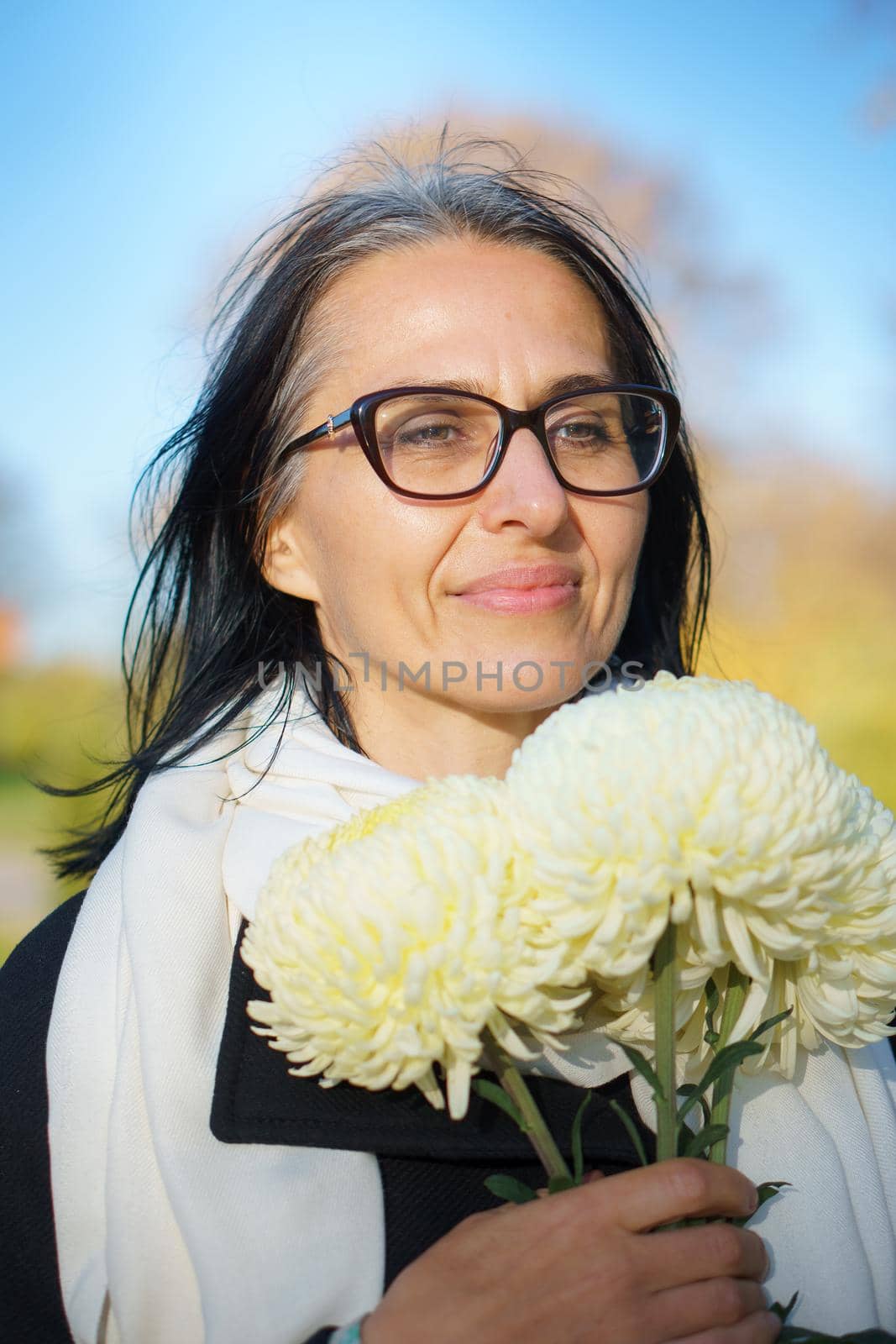 A beautiful middle-aged woman getting grey-haired in a dark coat in a spring town with a bouquet of flowers