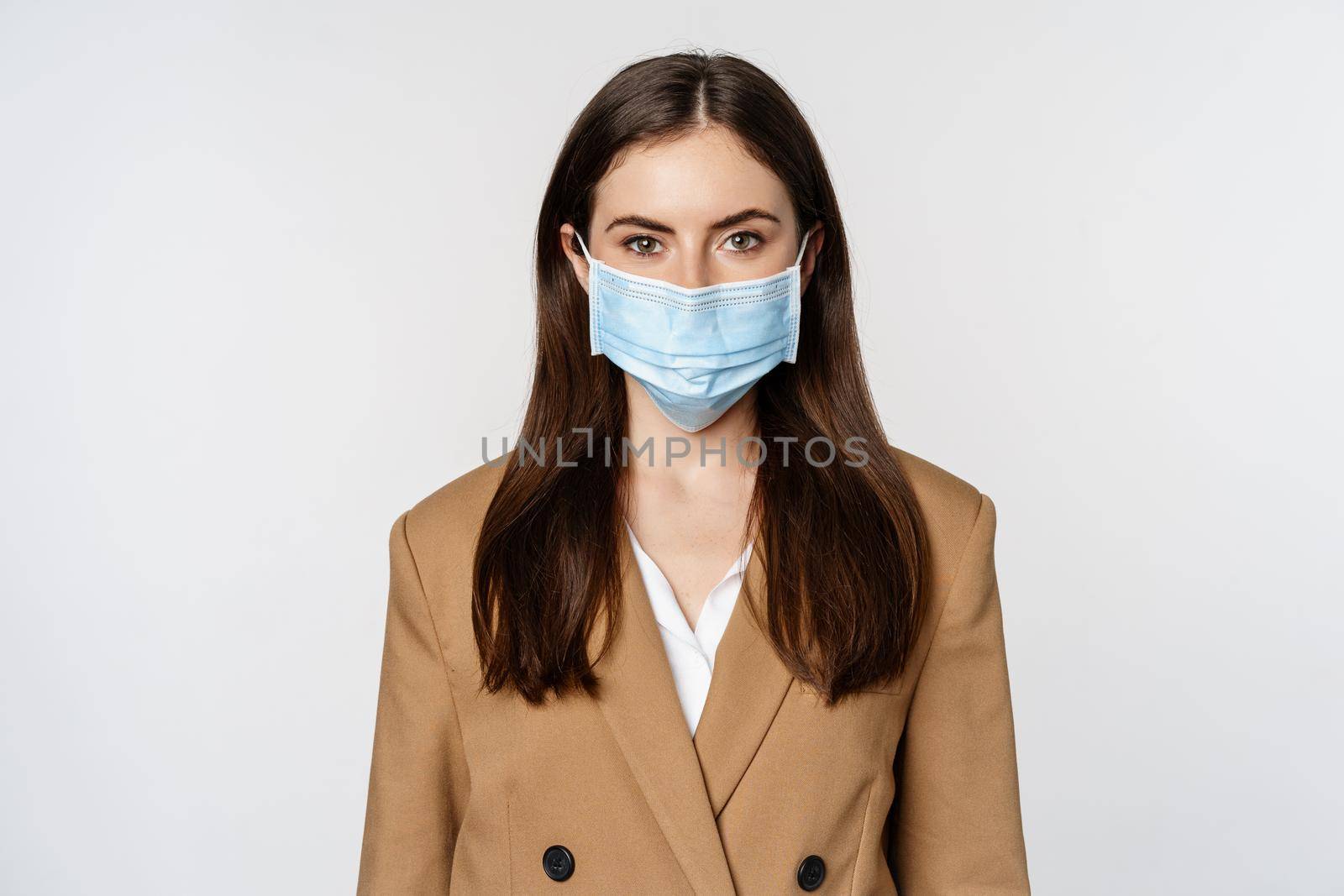 Workaplce and pandemic concept. Face portrait of businesswoman in medical mask and suit, looking serious at camera, going to work during covid-19.