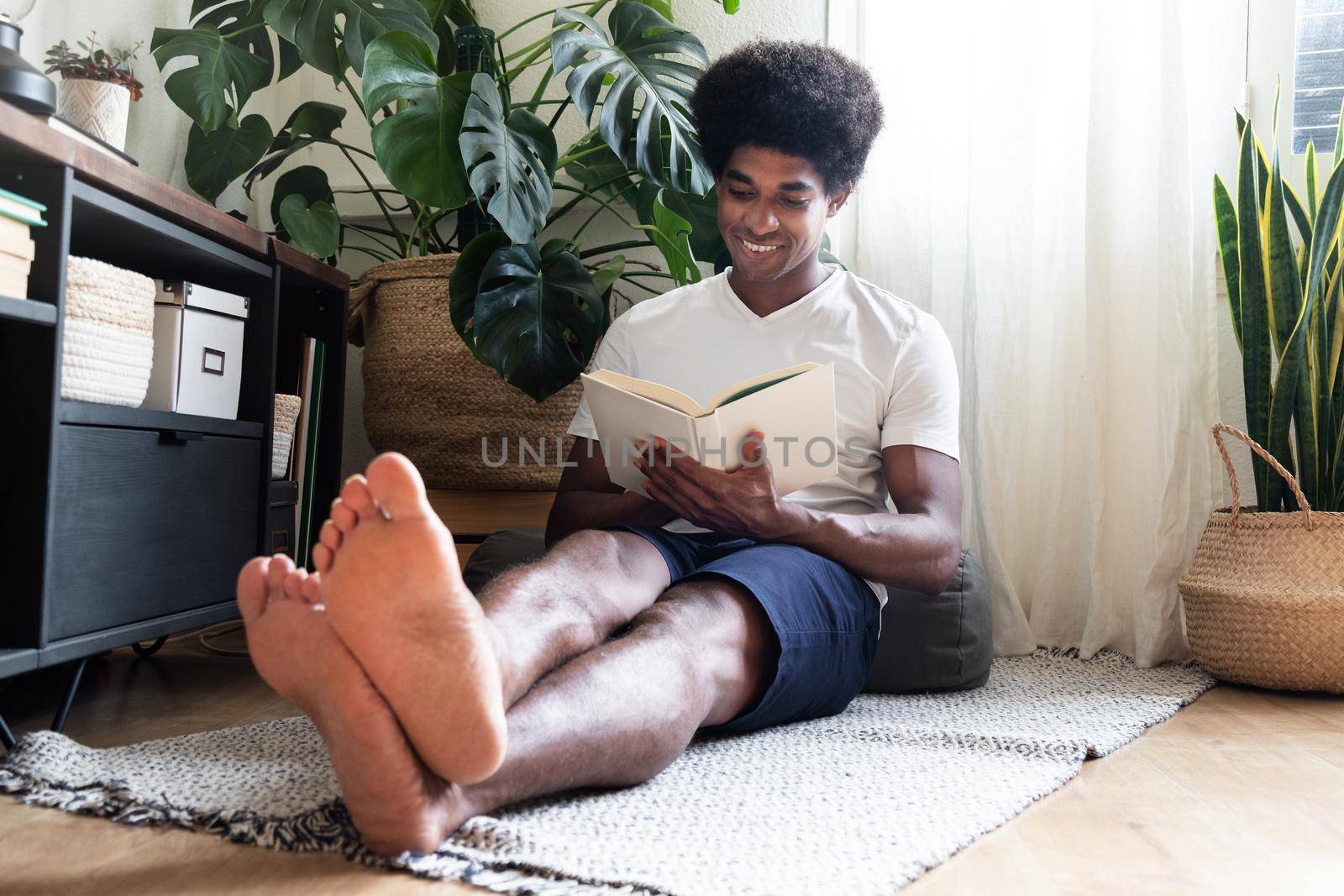 Happy and smiling young african american man reading a novel in cozy living room. At home concept.