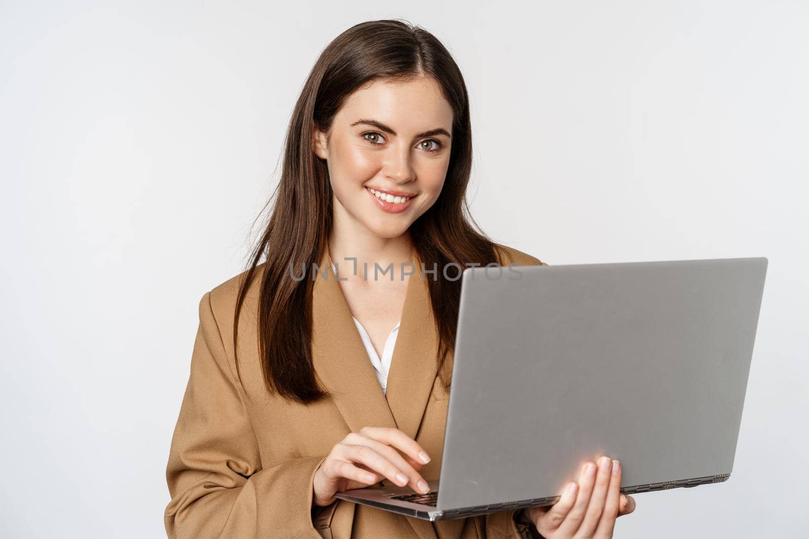 Portrait of corporate woman working with laptop, smiling and looking assertive, white background.