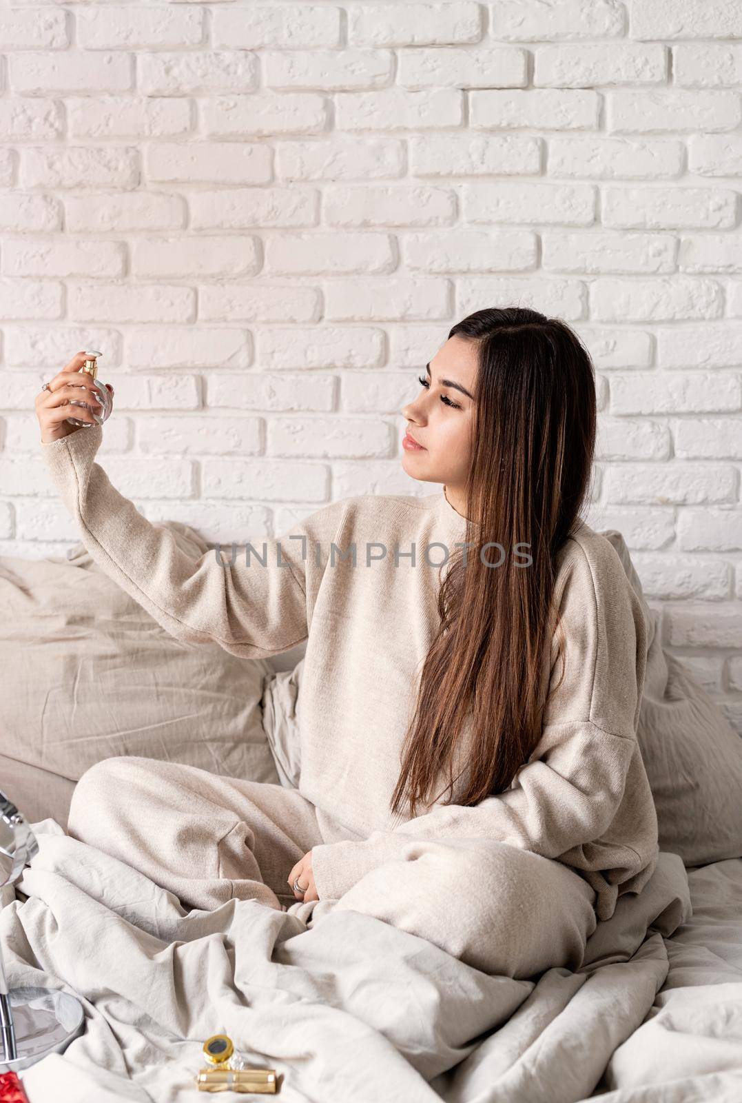 Valentine's day, Women's day. Brunette young caucasian Woman sitting on the bed making up applying perfume