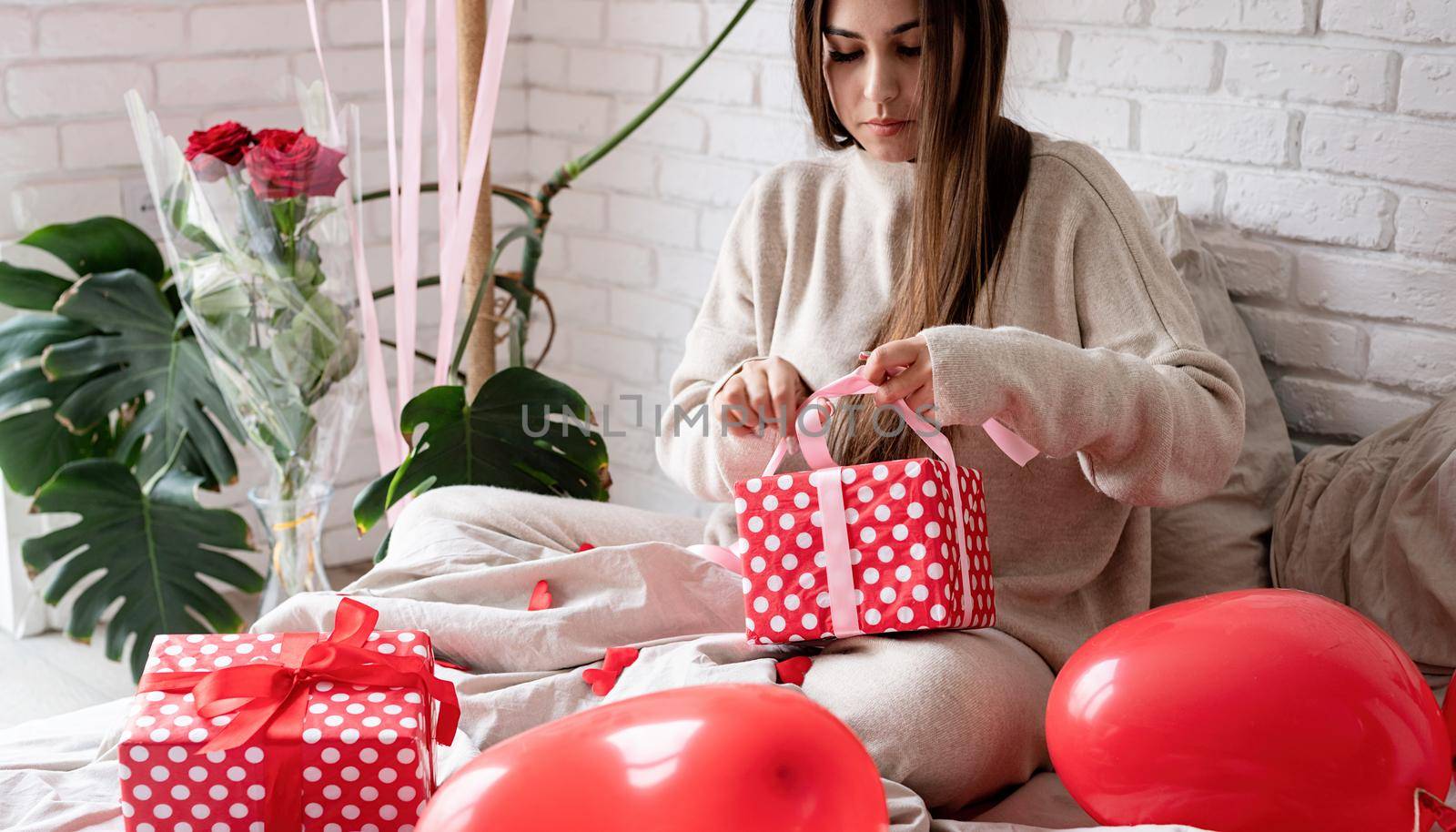 Valentine's day, Women's day. Young caucasian brunette woman sitting in the bed celebrating valentine day wrapping the gifts