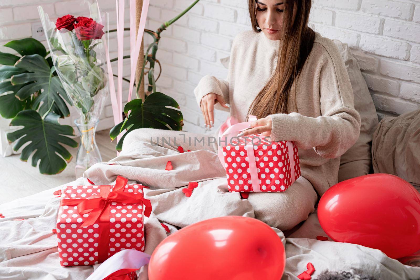 Young funny woman sitting in the bed celebrating valentine day wrapping the gifts by Desperada