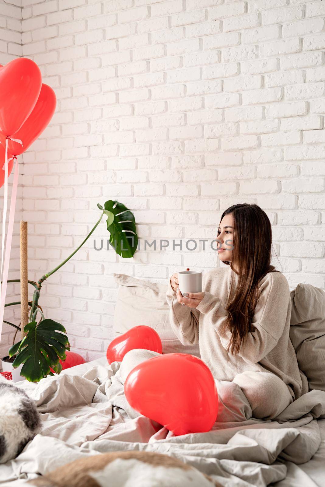 Young brunette woman sitting in the bed celebrating valentine day holding cup of coffee by Desperada