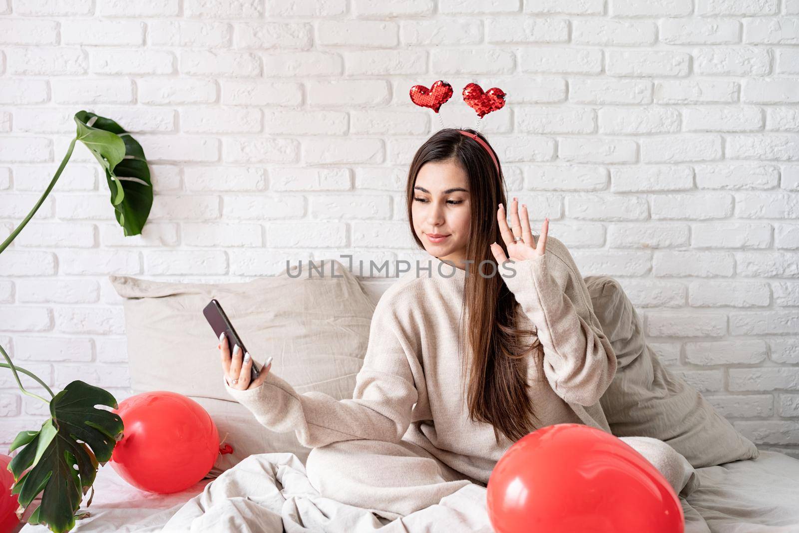 Valentine's day, Women's day. Young funny woman sitting in the bed celebrating valentine day chatting using mobile phone