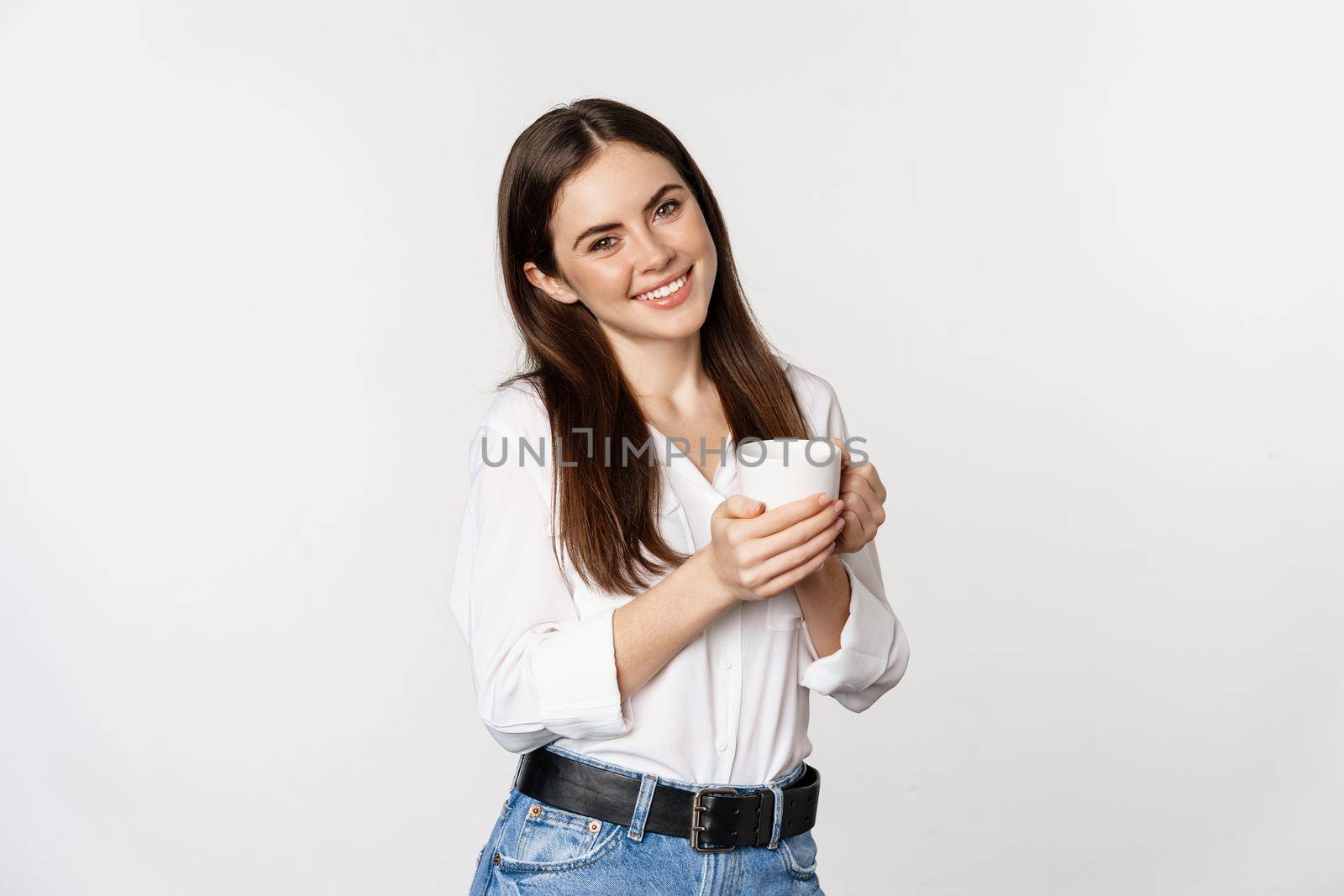 Corporate woman standing with coffee tea mug and smiling, drinking from cup, standing happy against white background.