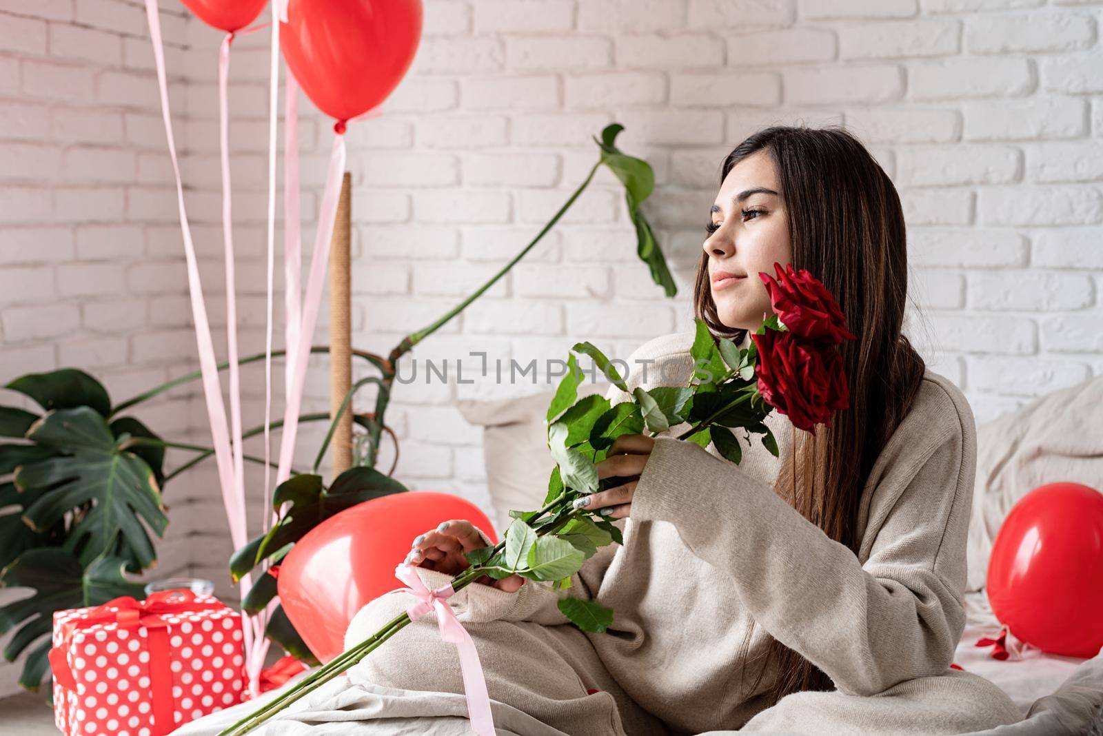 Young beautiful woman sitting in the bed celebrating valentine day holding red roses by Desperada