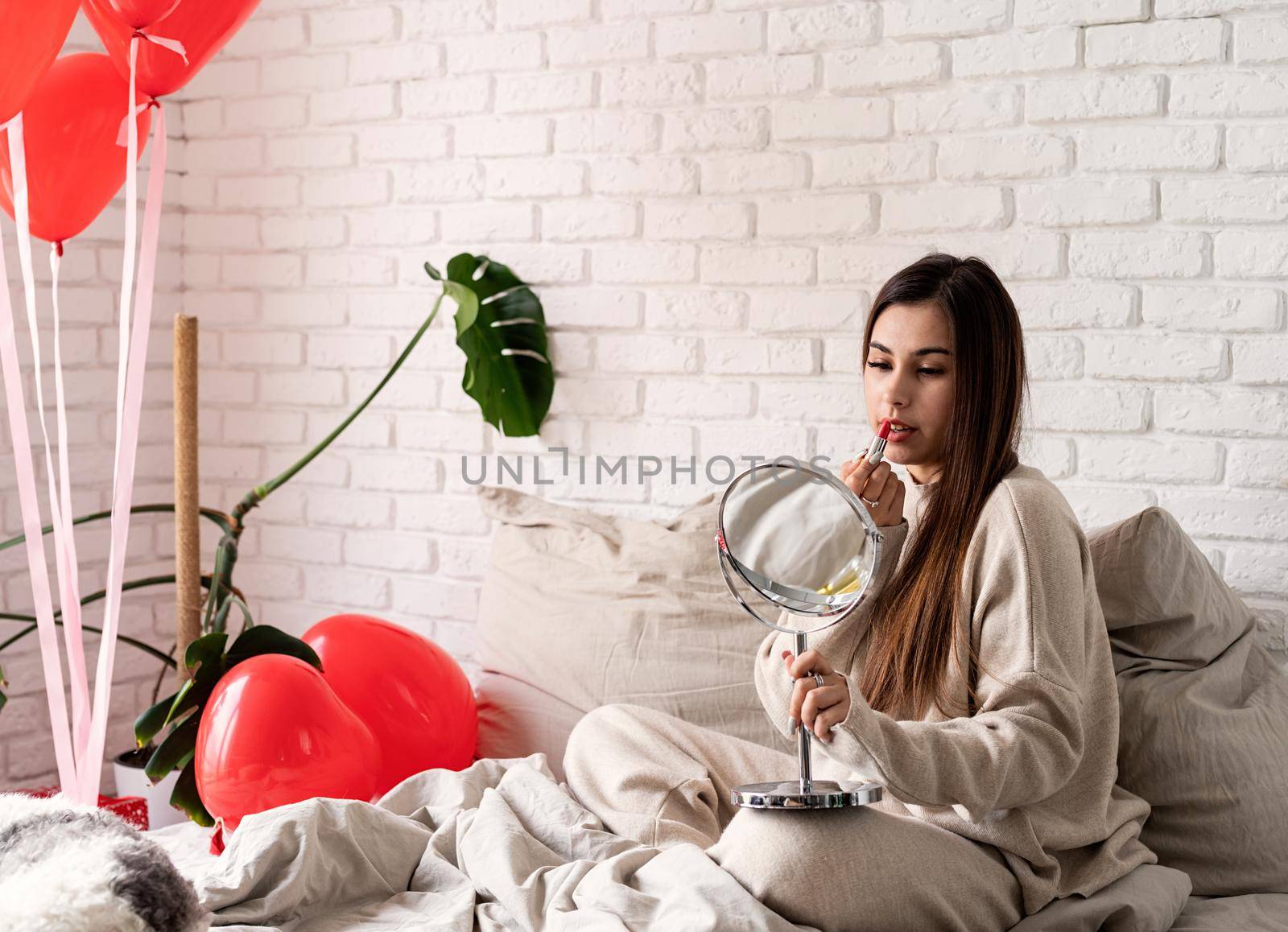 Valentine's day, Women's day. Brunette young caucasian Woman sitting on the bed making up coloring lips