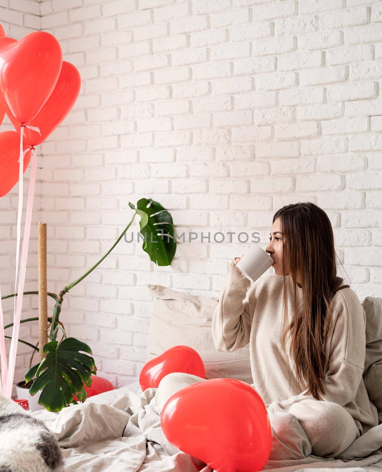 Young brunette woman sitting in the bed celebrating valentine day holding cup of coffee by Desperada