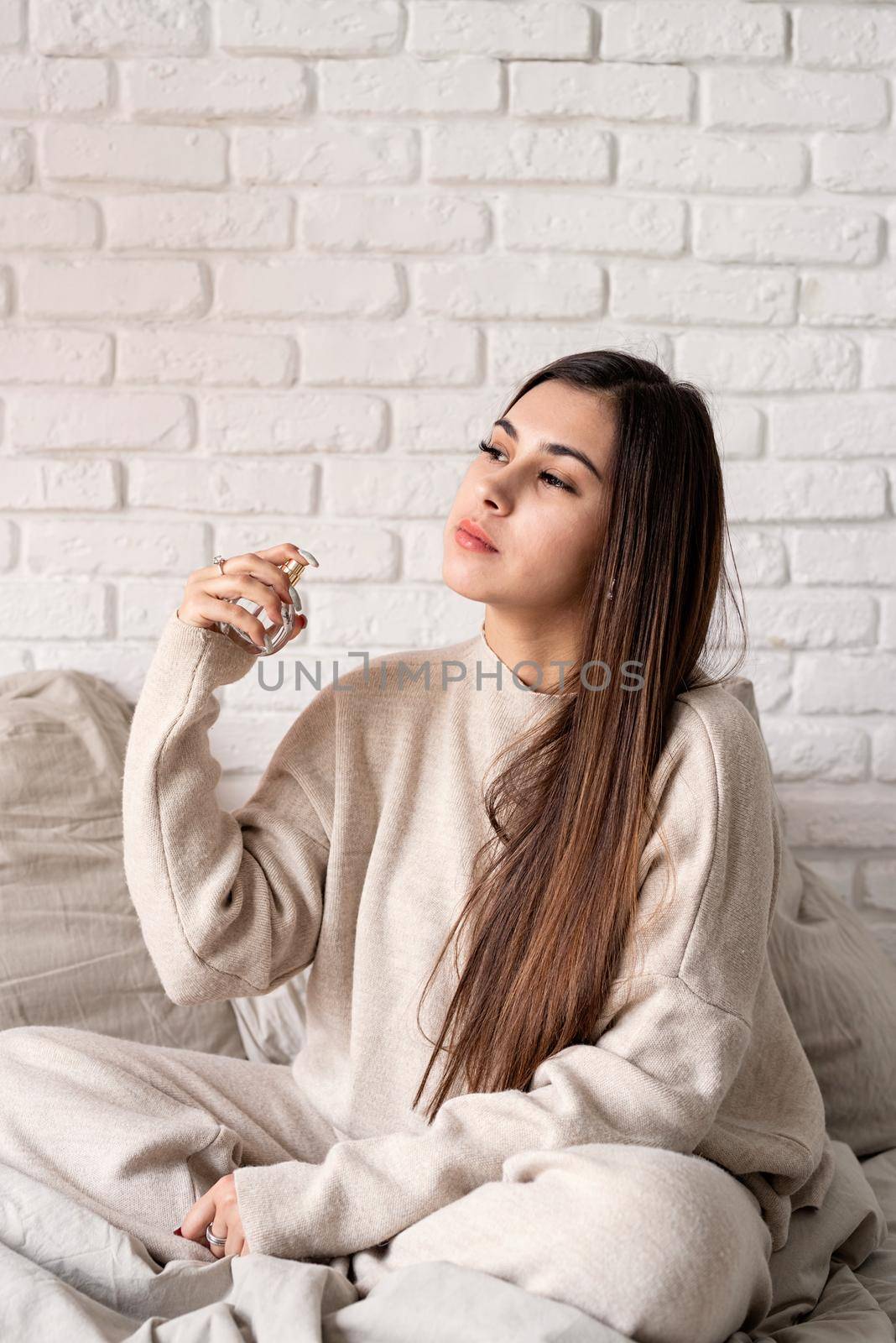 Valentine's day, Women's day. Brunette young caucasian Woman sitting on the bed making up applying perfume