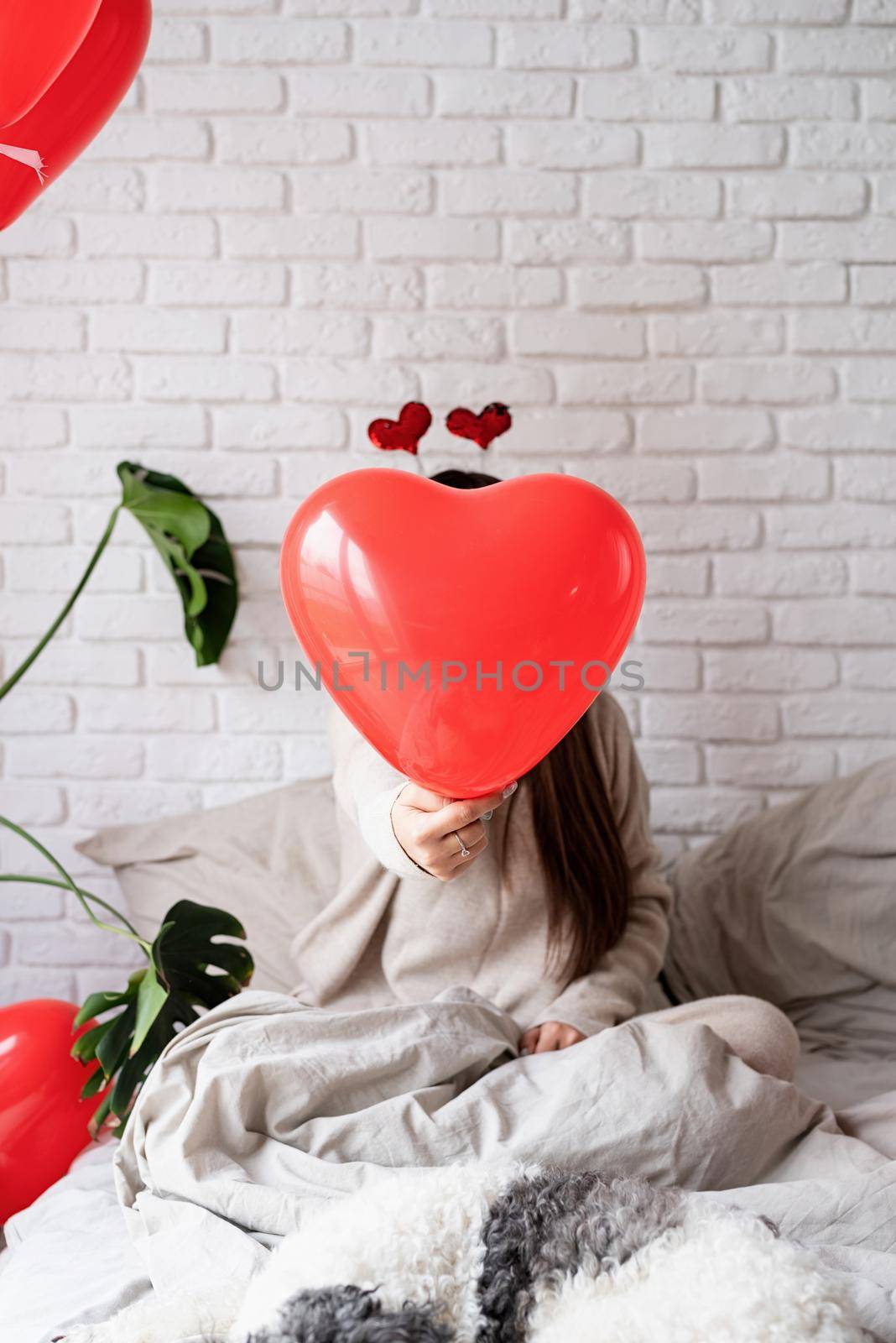 Valentine's day, Women's day. Young funny woman sitting in the bed celebrating valentine day holding balloons