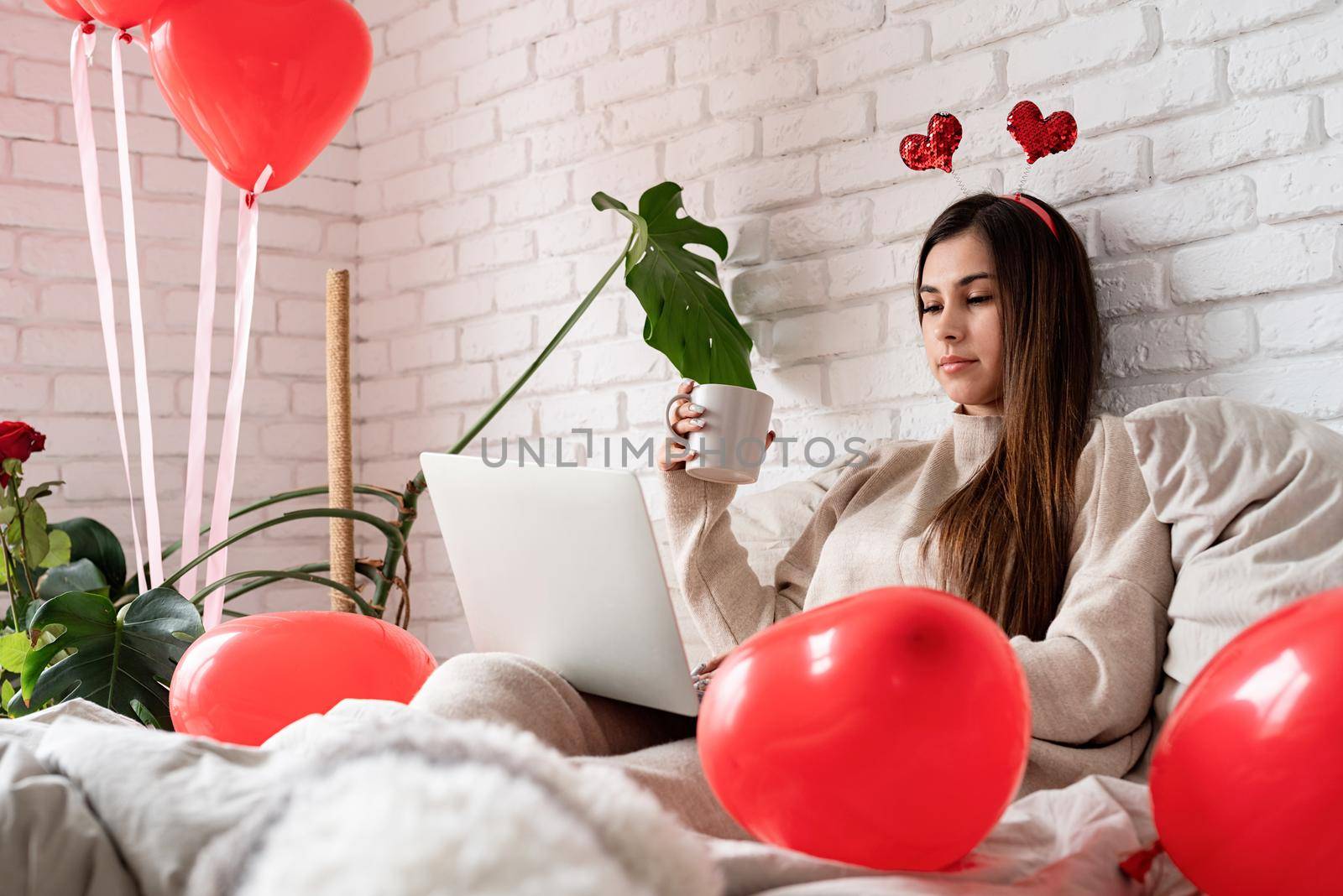 Valentine's day, Women's day. Young caucasian brunette woman sitting in the bed celebrating valentine day working on laptop online