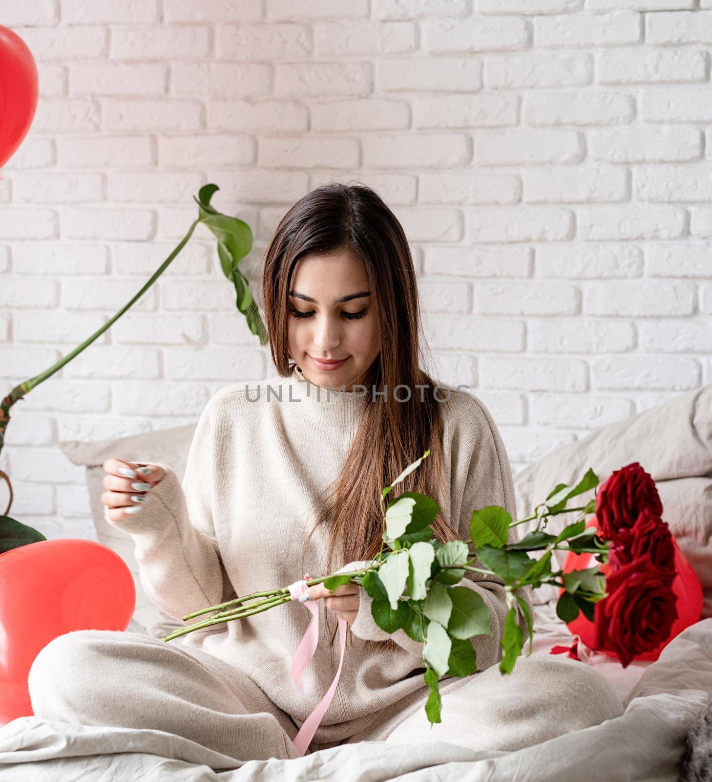 Young beautiful woman sitting in the bed celebrating valentine day holding red roses by Desperada