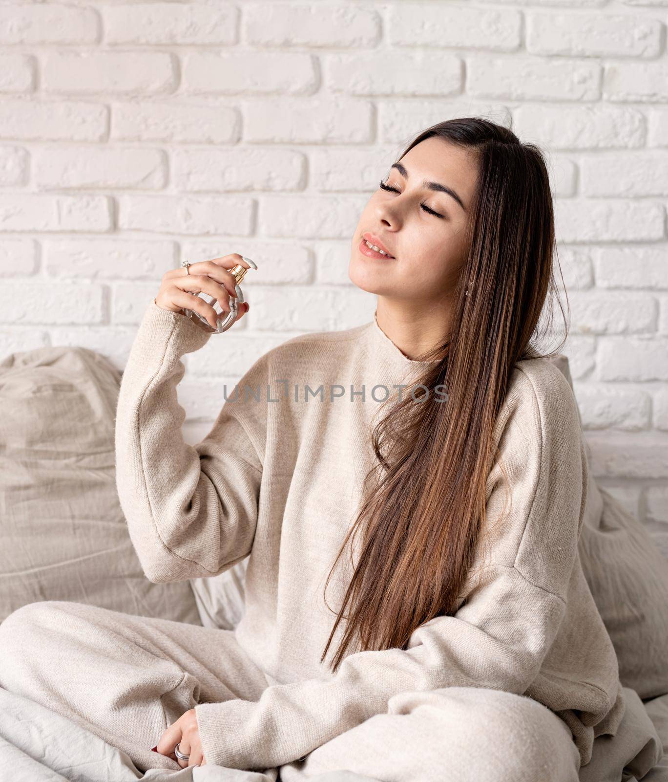 Valentine's day, Women's day. Brunette young caucasian Woman sitting on the bed making up applying perfume