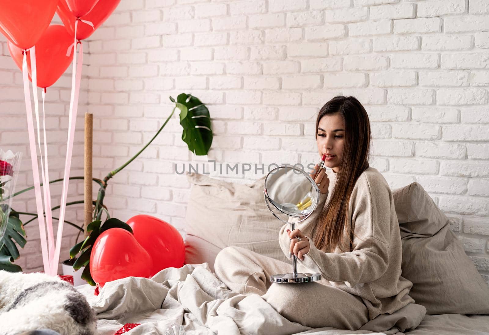 Valentine's day, Women's day. Brunette young caucasian Woman sitting on the bed making up coloring lips