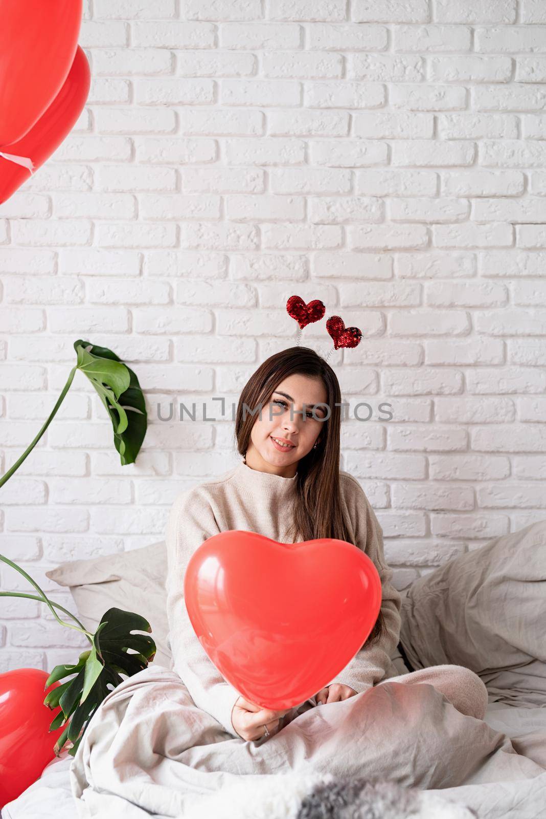 Valentine's day, Women's day. Young funny woman sitting in the bed celebrating valentine day holding balloons