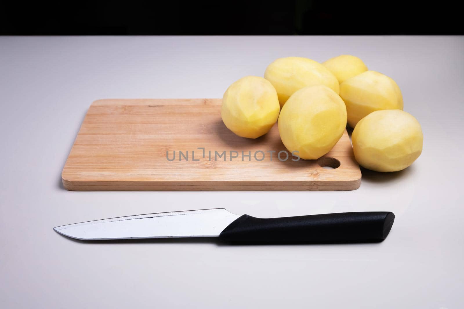 Peeled potatoes on a wooden cutting board next to a kitchen knife. Home cooking vegetables. Healthy food by yanik88