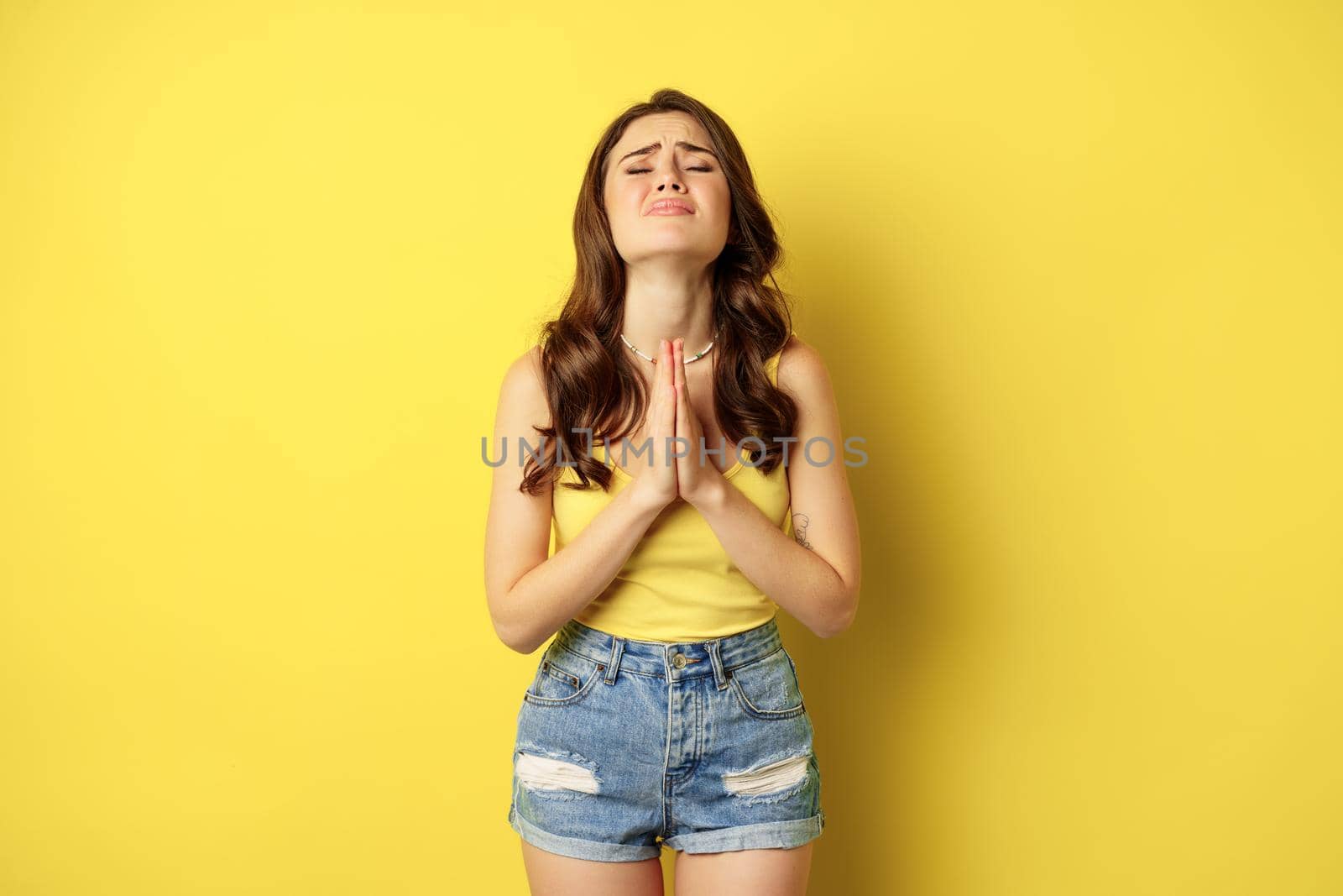 Desperate sad woman asking for help, begging with pray, need something, supplicating or praying, standing over yellow background. copy space