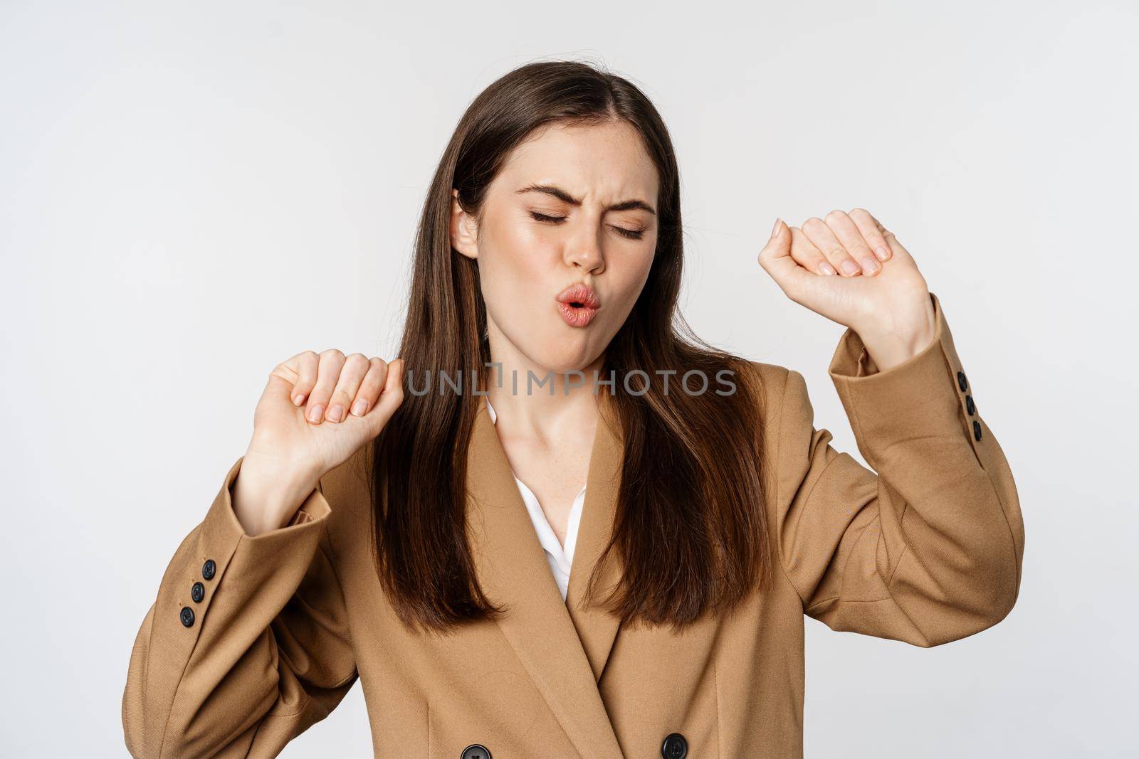 Successful businesswoman, saleswoman dancing and having fun, wearing office suit, posing over white background.