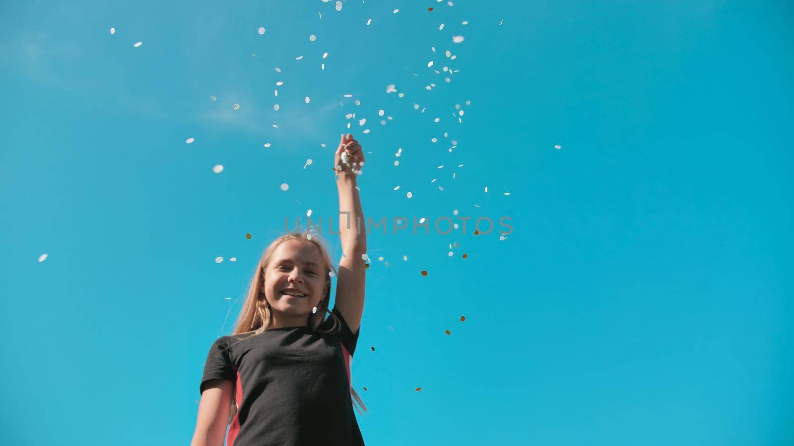 Teen girl scatters a multi-colored confetti on a background of blue sky