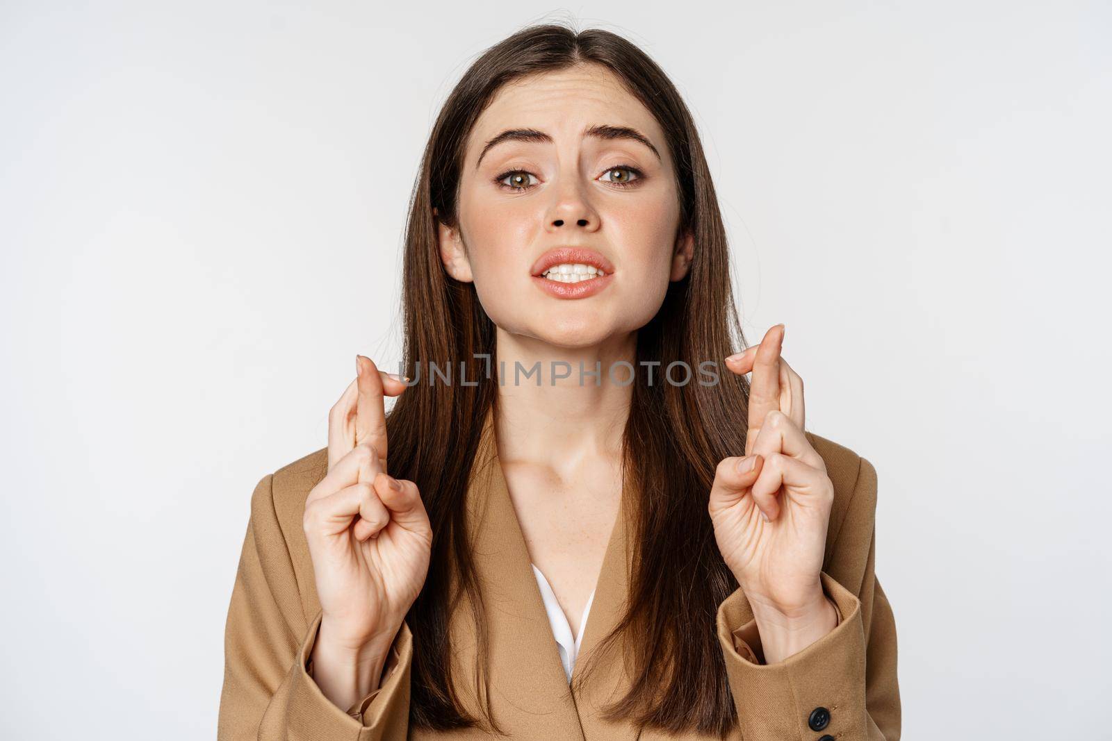 Hopeful saleswoman, corporate woman cross fingers and praying, yearning to achieve smth, standing in suit over white background. Copy space