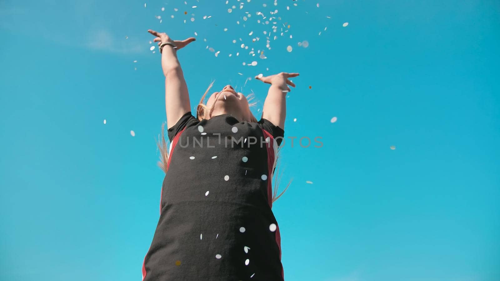 Success concept. Teen girl throws a multi-colored confetti into the blue sky. by DovidPro