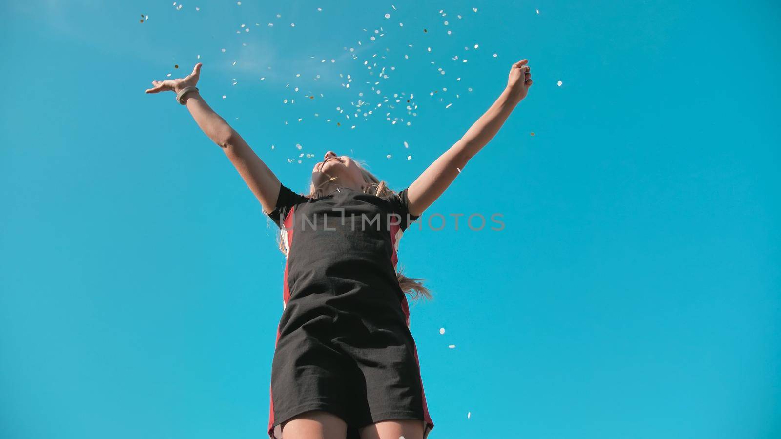 Success concept. Teen girl throws a multi-colored confetti into the blue sky. by DovidPro
