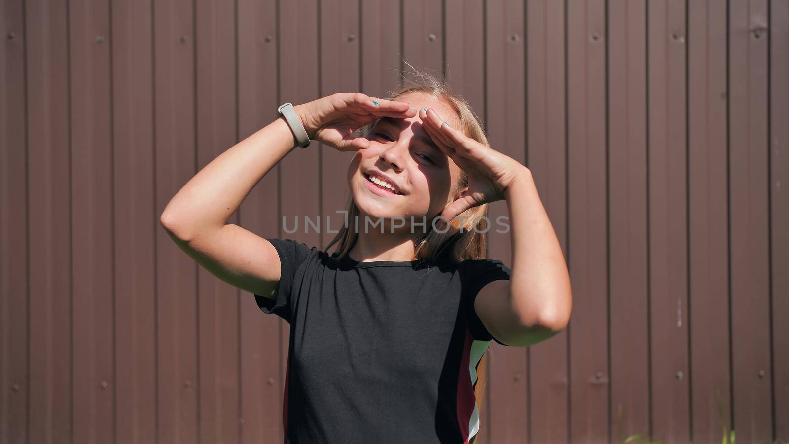 Teen girl closes her eyes from the sun with her hands on a brown background. by DovidPro