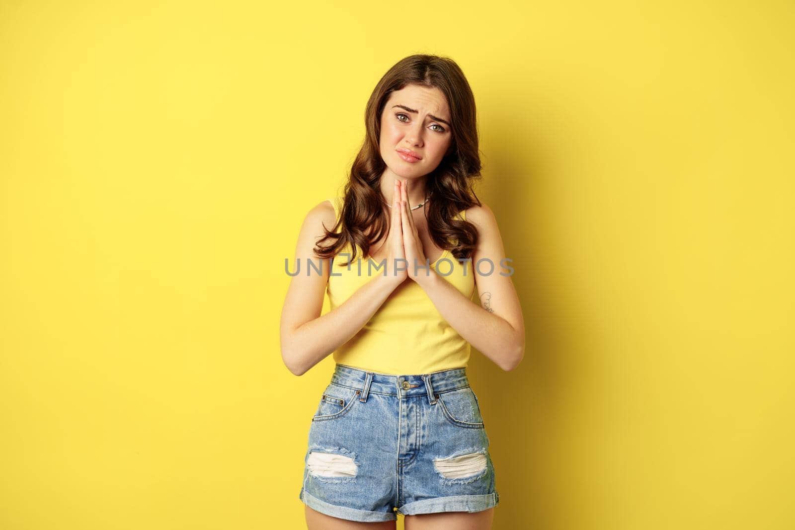 Desperate sad woman asking for help, begging with pray, need something, supplicating or praying, standing over yellow background. copy space