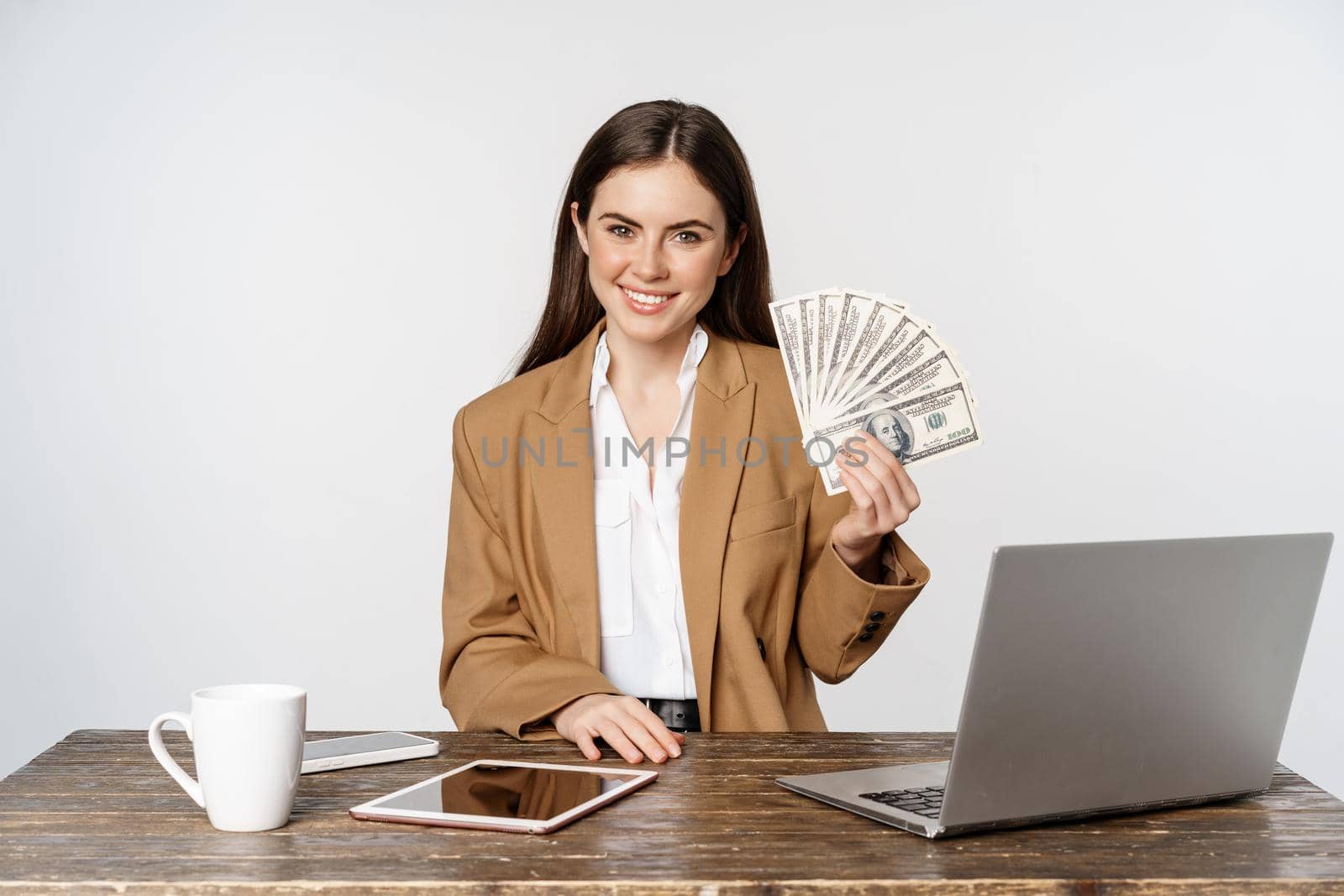 Portrait of businesswoman sitting in office with money, working and making profit income, posing happy against white studio background.